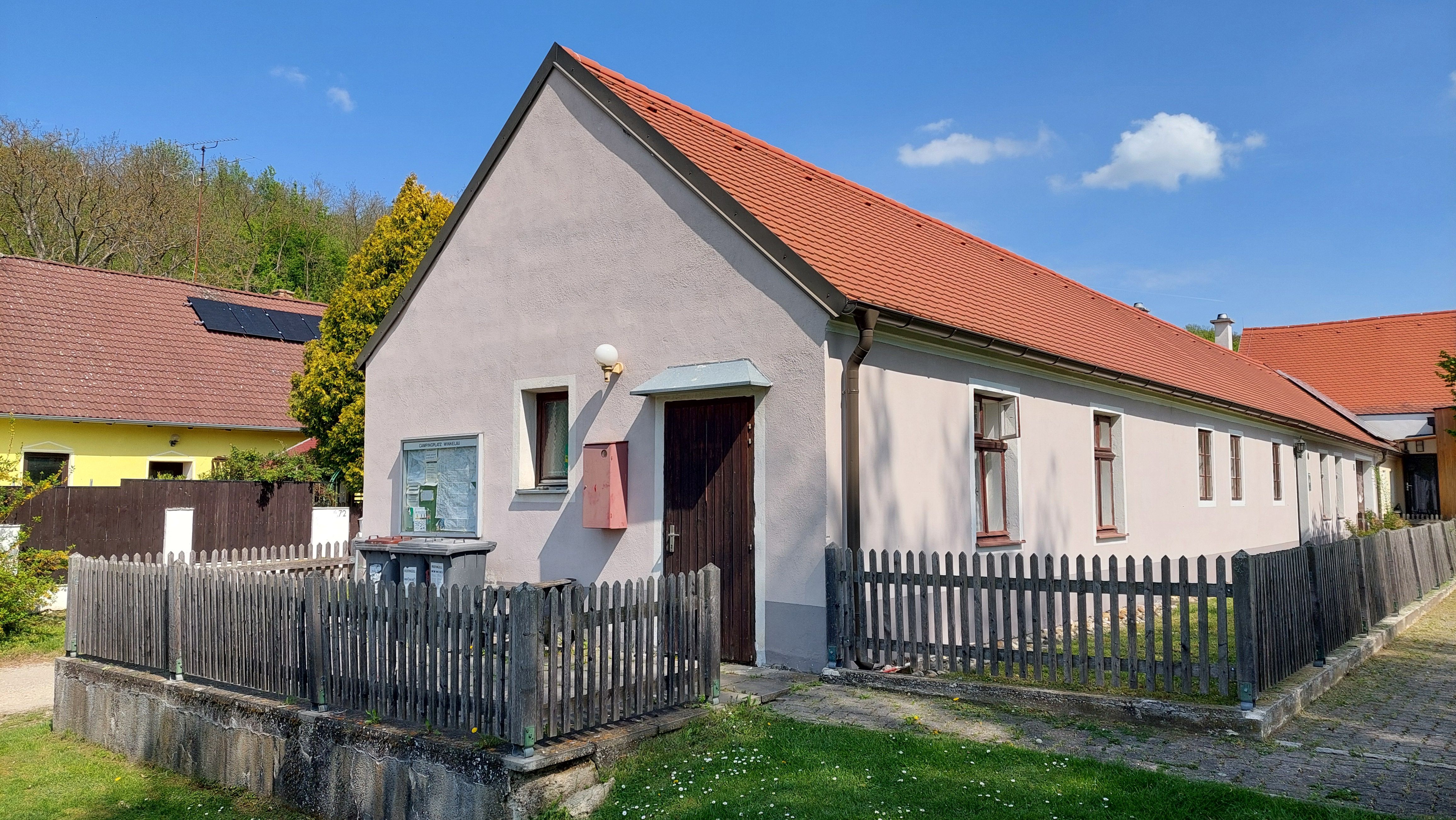 Ein langes, einstöckiges Haus mit rotem Dach und Holzzaun, umgeben von grünem Gras und blauem Himmel.