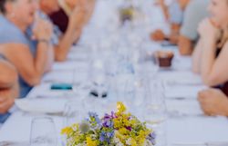 Eine lange Tafel, geschmückt mit bunten Blumen, lädt zu einem geselligen Abendessen ein. Umgeben von der malerischen Kellergasse „Alte Geringen“ genießen die Gäste die kulinarischen Köstlichkeiten der Region. Die Atmosphäre ist geprägt von fröhlichem Lachen und dem Duft von frisch zubereiteten Speisen.