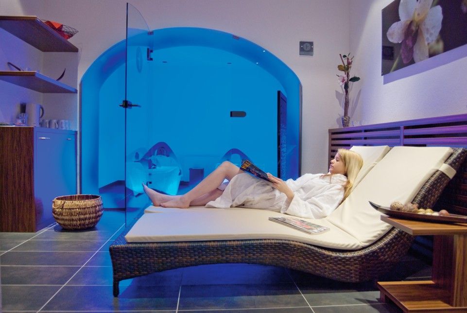 Frau entspannt auf einer Liege im Wellnessbereich mit blauer Beleuchtung.