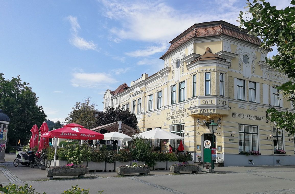 Historisches Gebäude mit Café und Terrasse, umgeben von Sonnenschirmen und Pflanzen.