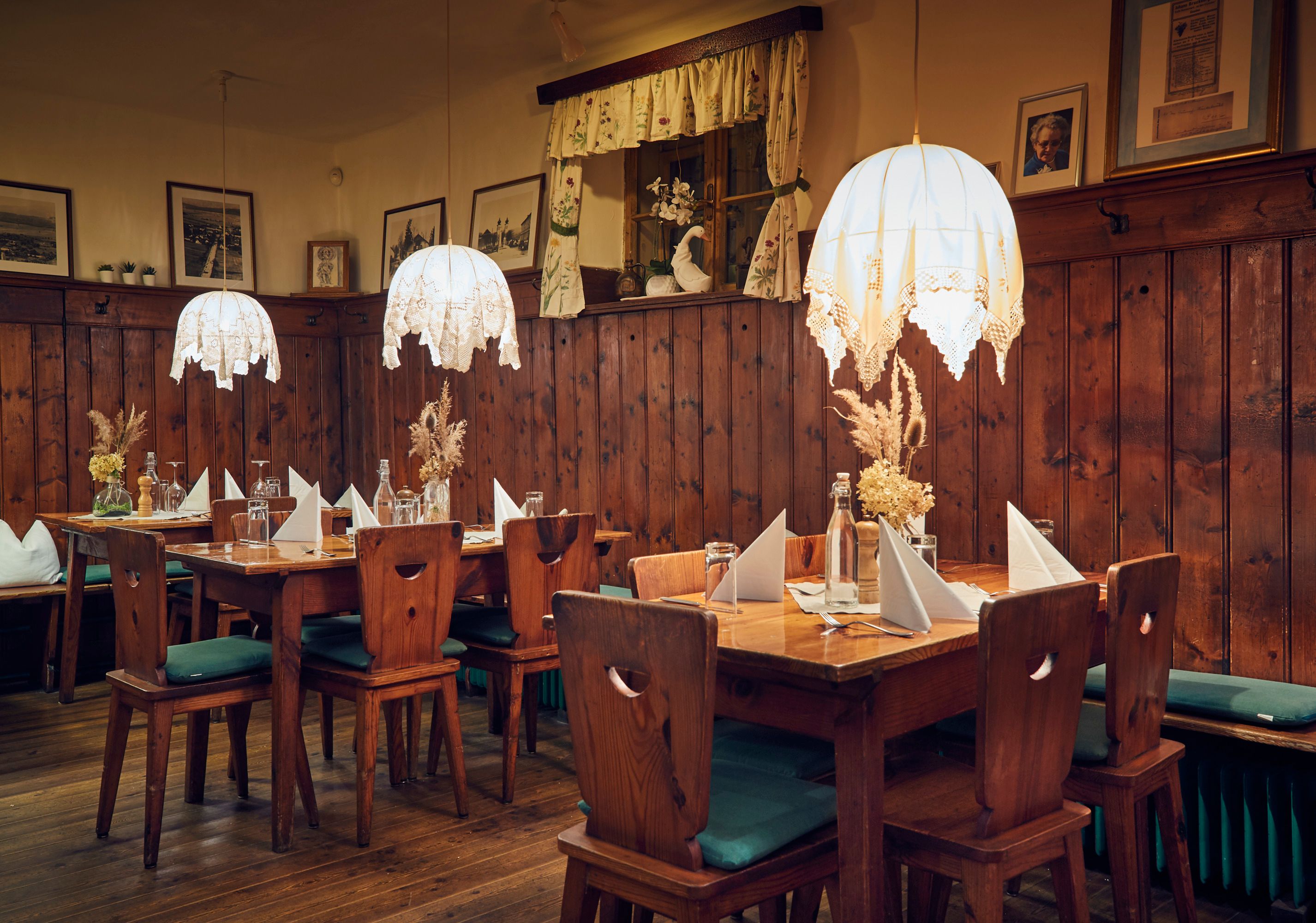 Gemütliche Stube mit Holzmöbeln, Tischdekoration und hängenden Lampen.