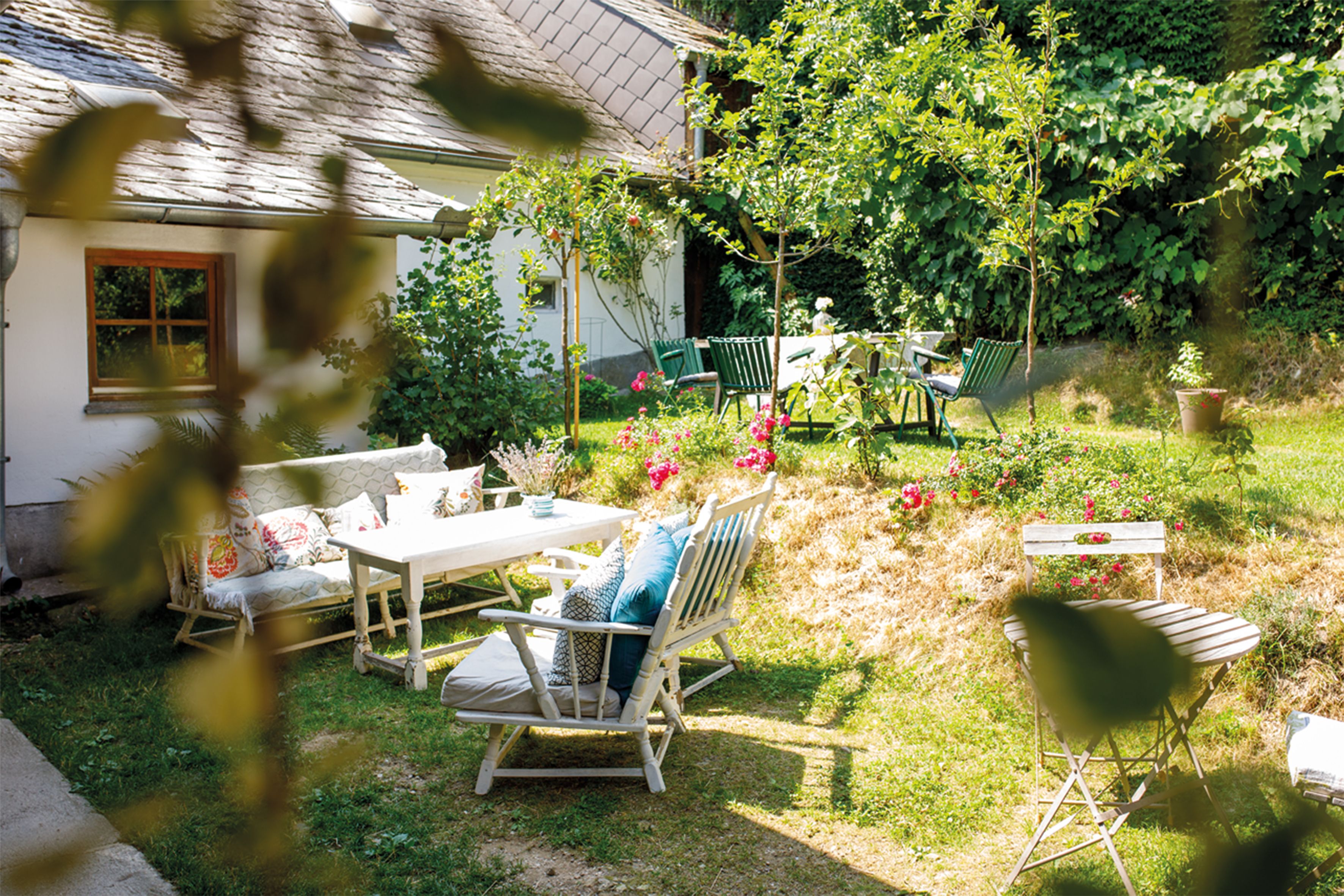 Ein gemütlicher Innenhof mit Gartenmöbeln, Blumen und Bäumen, umgeben von einem Haus und grüner Vegetation.