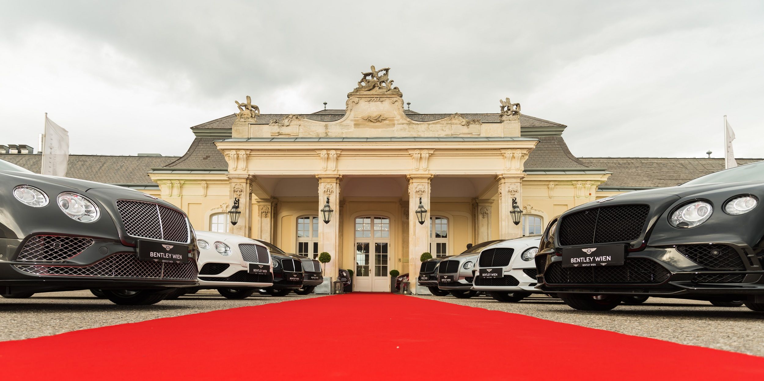 Luxusautos vor einem historischen Gebäude mit rotem Teppich.