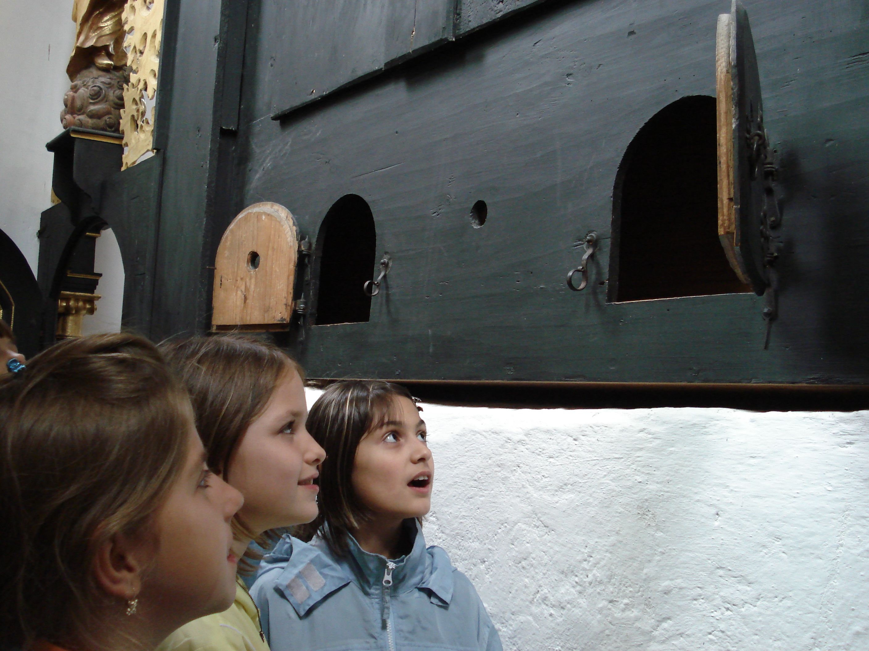 Drei Kinder betrachten neugierig eine Wand mit kleinen Türen.