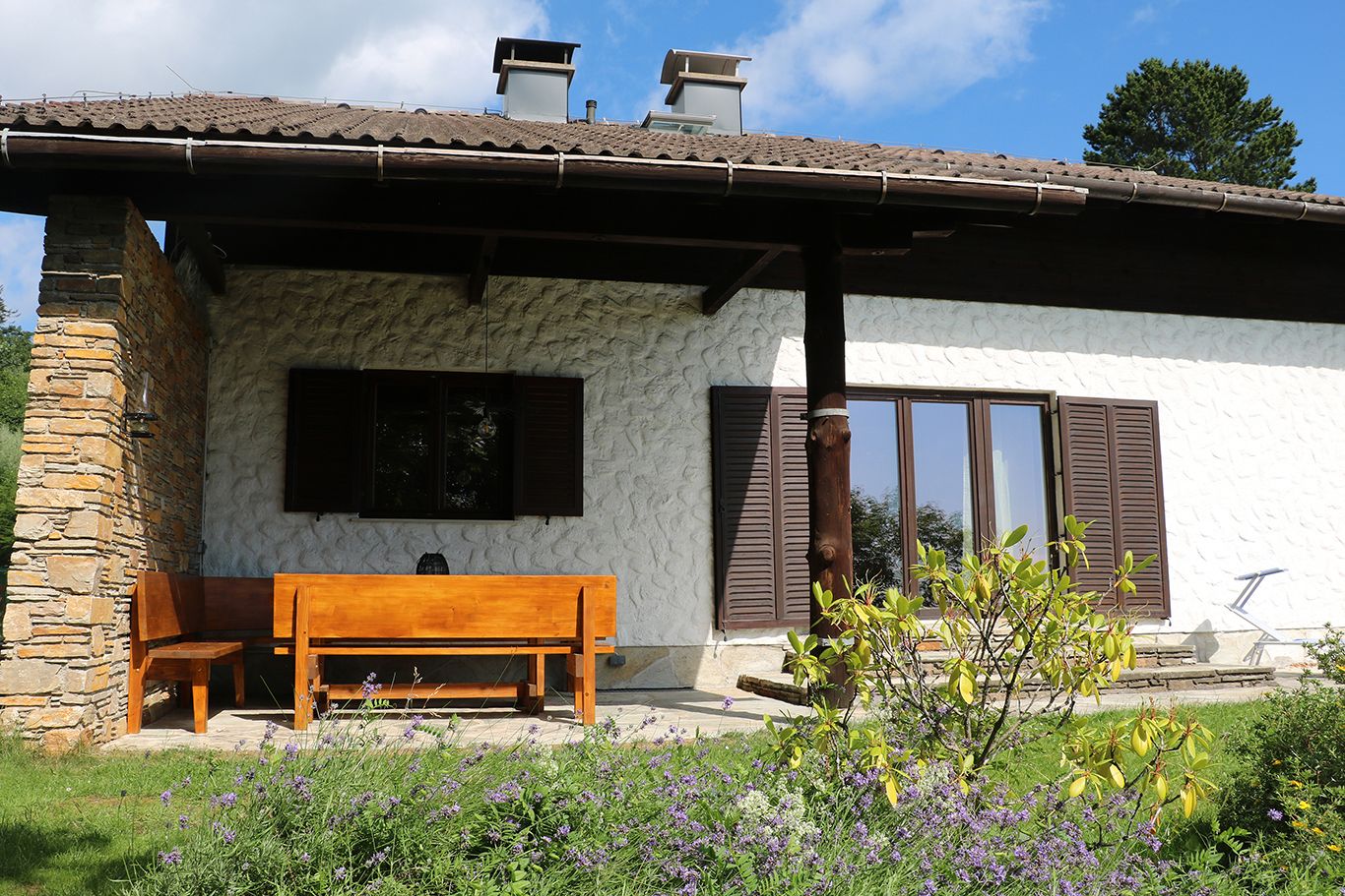 Ein Haus mit einer Holzsitzgruppe auf der Terrasse, umgeben von einem Garten mit Blumen.