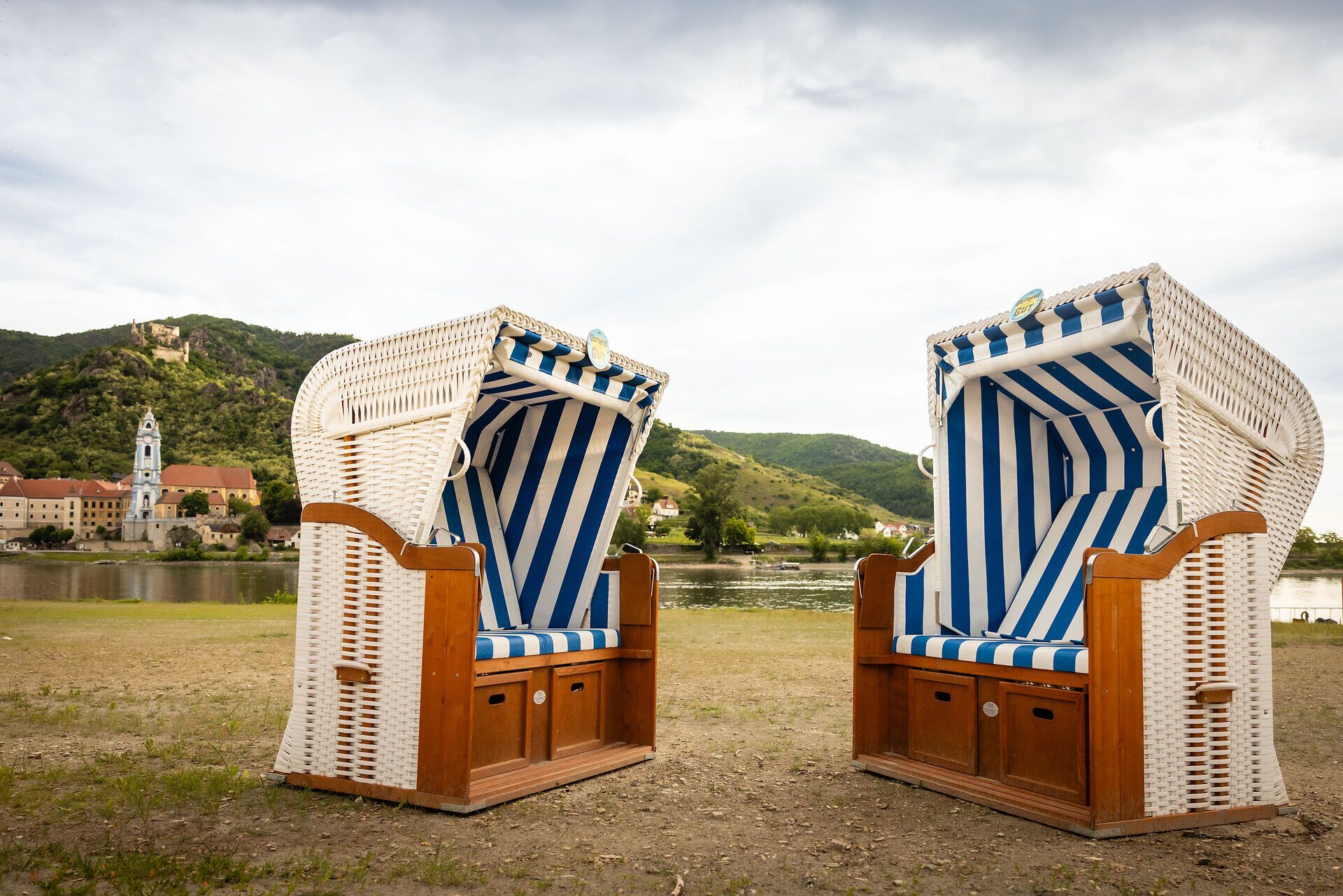 Eine Frau liegt auf einer Luftmatratze im Wasser, mit Blick auf die Stadt Dürnstein und die umliegenden Hügel.