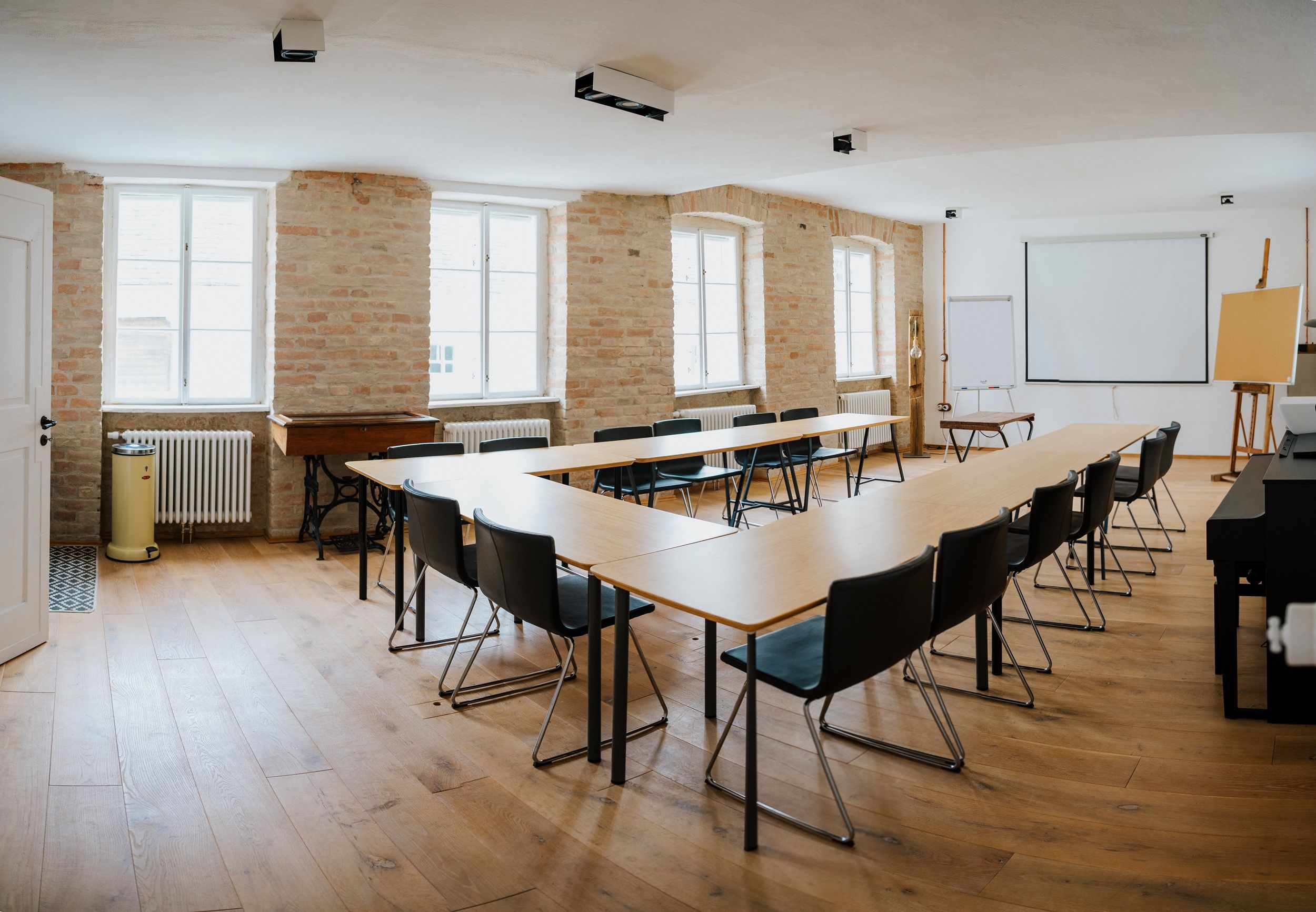 Ein heller Seminarraum mit U-förmiger Tischanordnung, Stühlen, Projektionsleinwand und Flipchart.