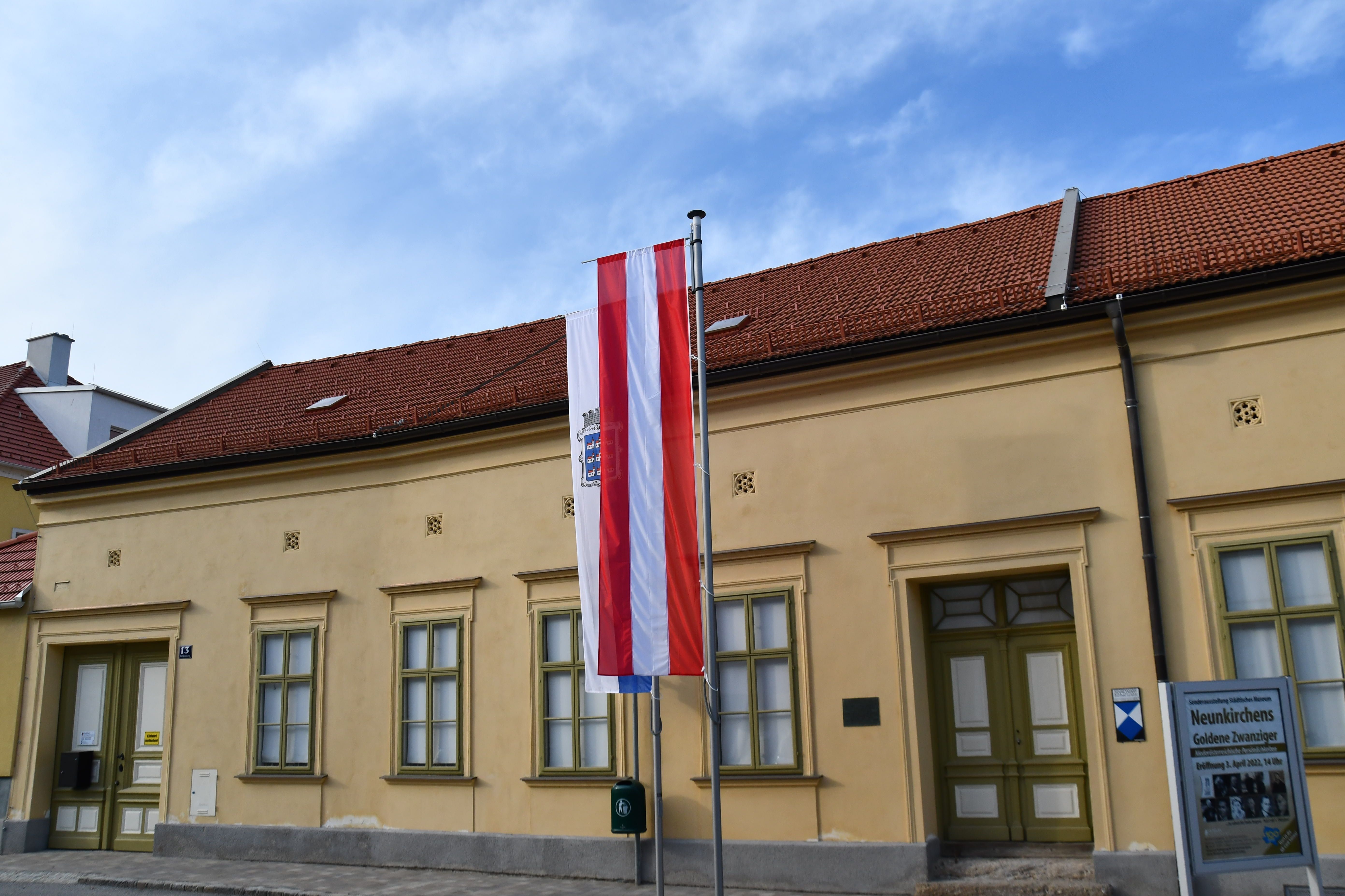 Außenansicht des Museums Neunkirchen mit österreichischer Flagge und Informationsschild.