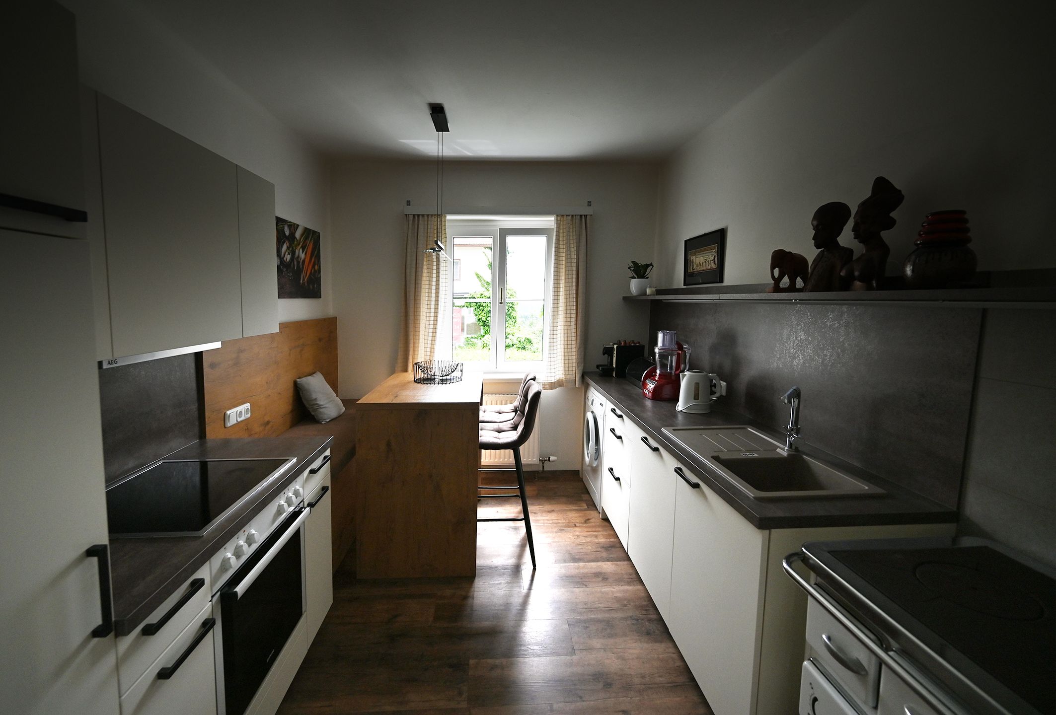 Moderne Küche mit Holz- und Metallakzenten, Esstisch am Fenster, Küchengeräte und Dekorationen auf Regalen.