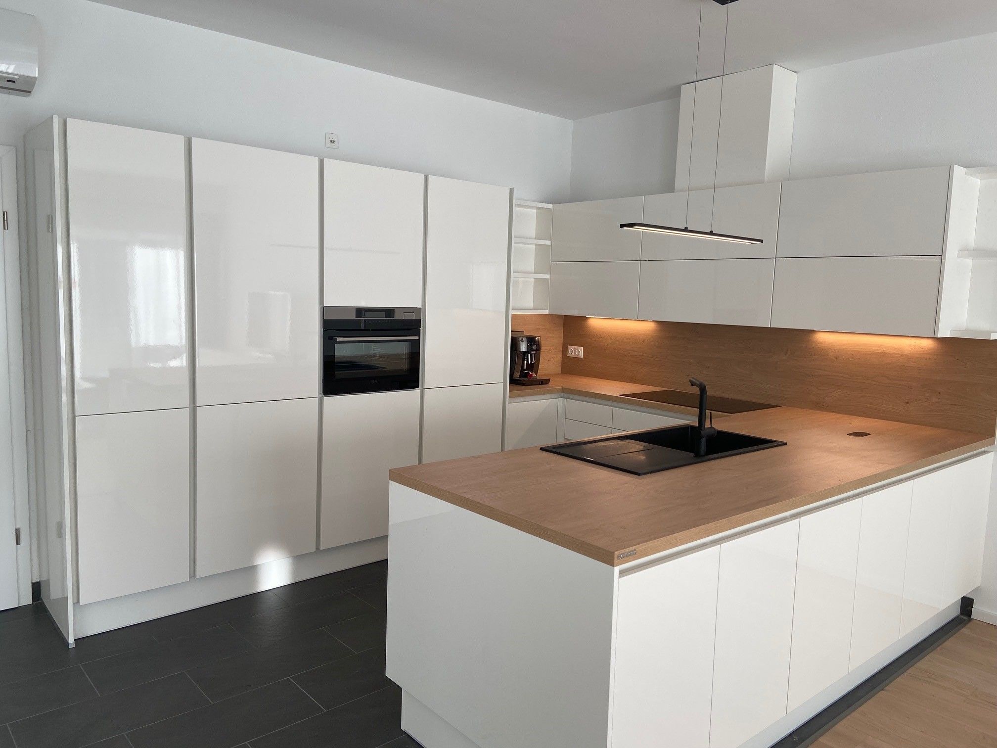 Moderne Küche mit weißen Hochglanzschränken, Holzarbeitsplatte und eingebautem Ofen.