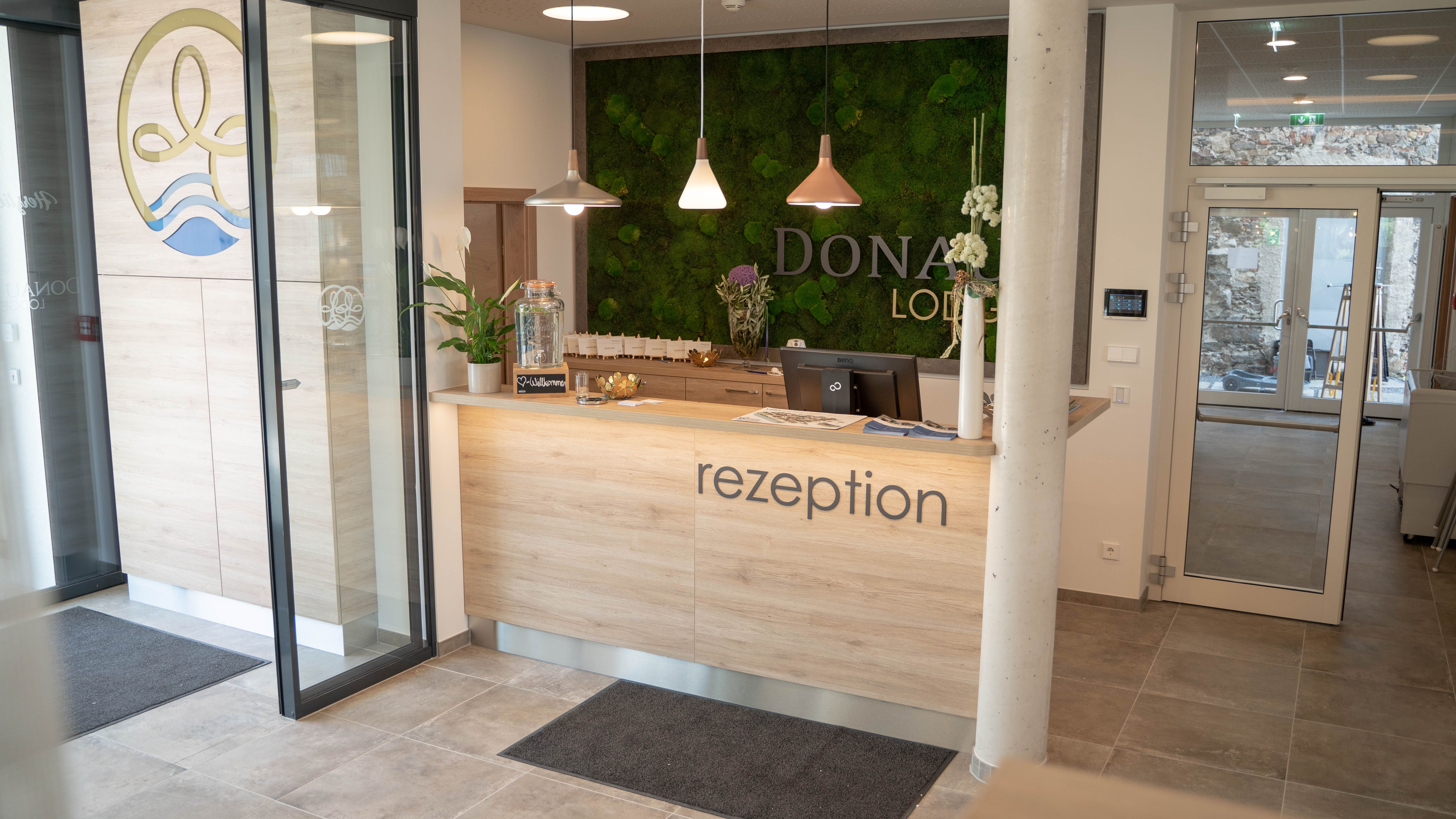 Rezeption mit Holztheke und grüner Mooswand im Hintergrund.