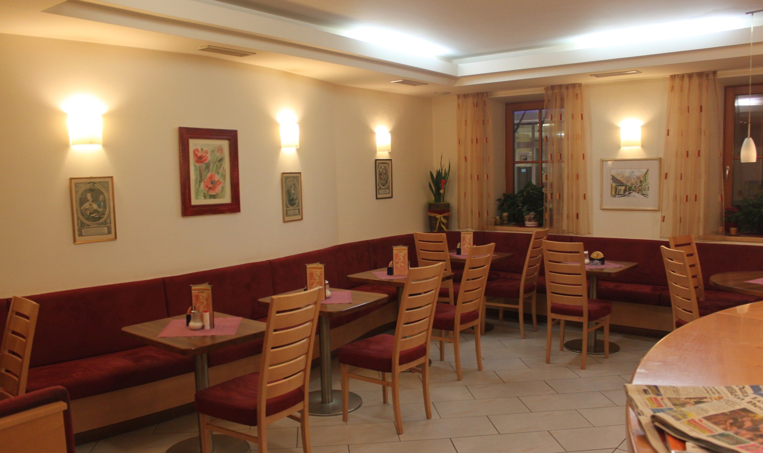 Innenansicht eines gemütlichen Cafés mit roten Sitzbänken und Holztischen.