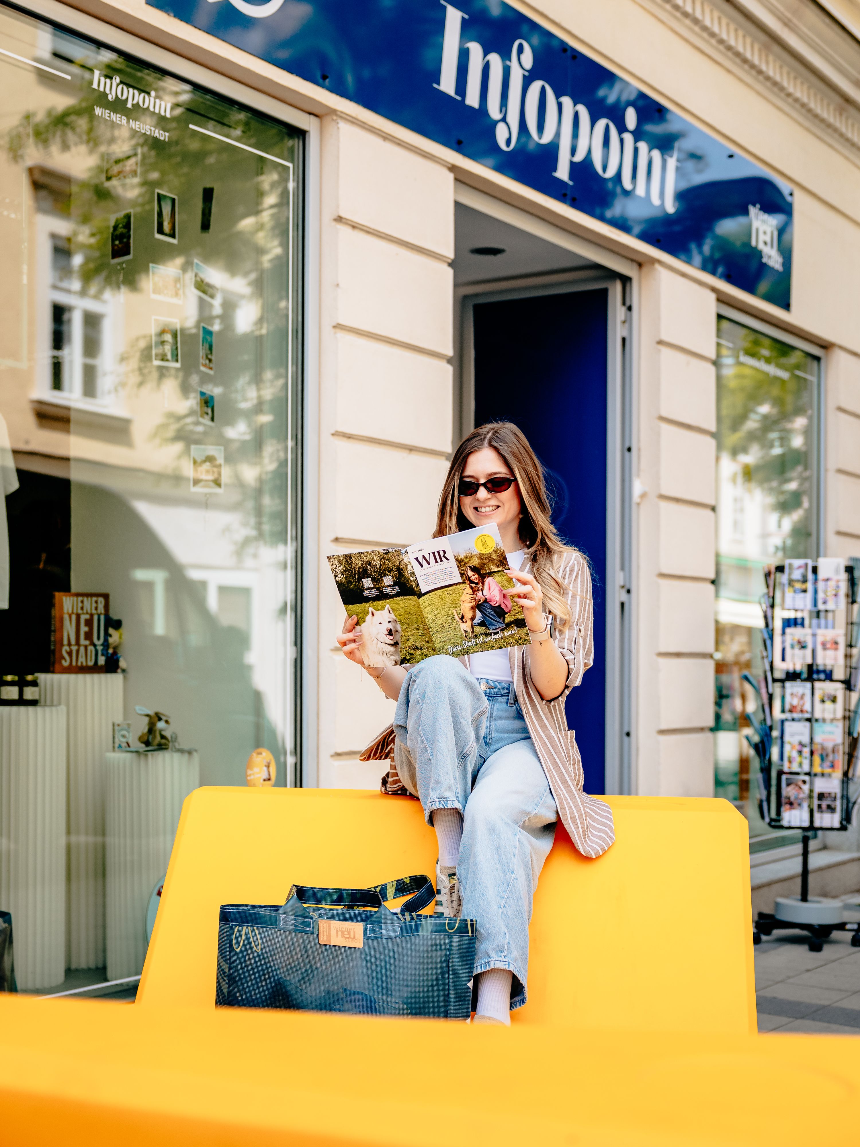 Bunte Enzis vor dem Infopoint, auf dem eine Frau ein Magazin der Stadt liest