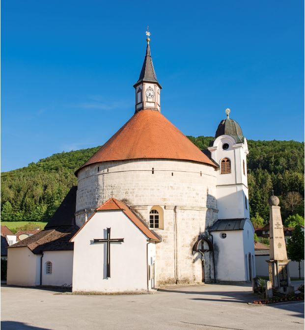 Pfarrkirche Scheiblingkirchen mit rundem Turm und rotem Dach vor blauem Himmel.