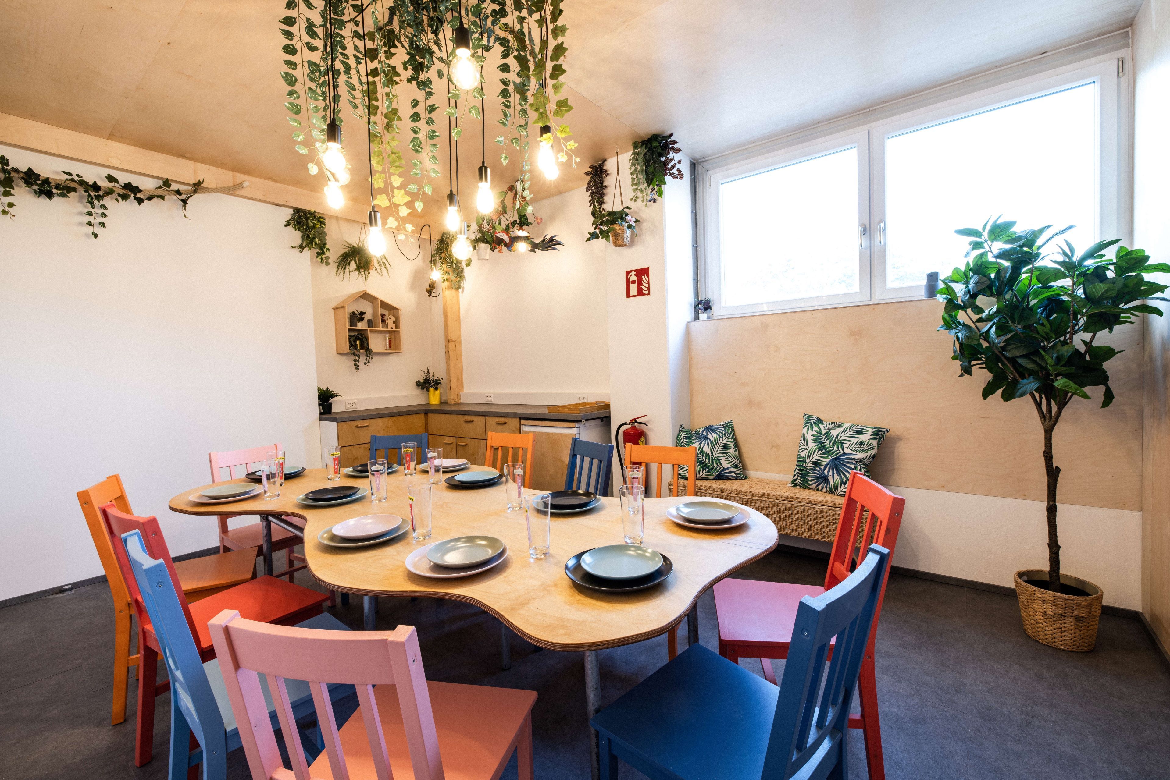 Ein gemütlicher Raum mit einem Tisch, umgeben von bunten Stühlen und Pflanzen.