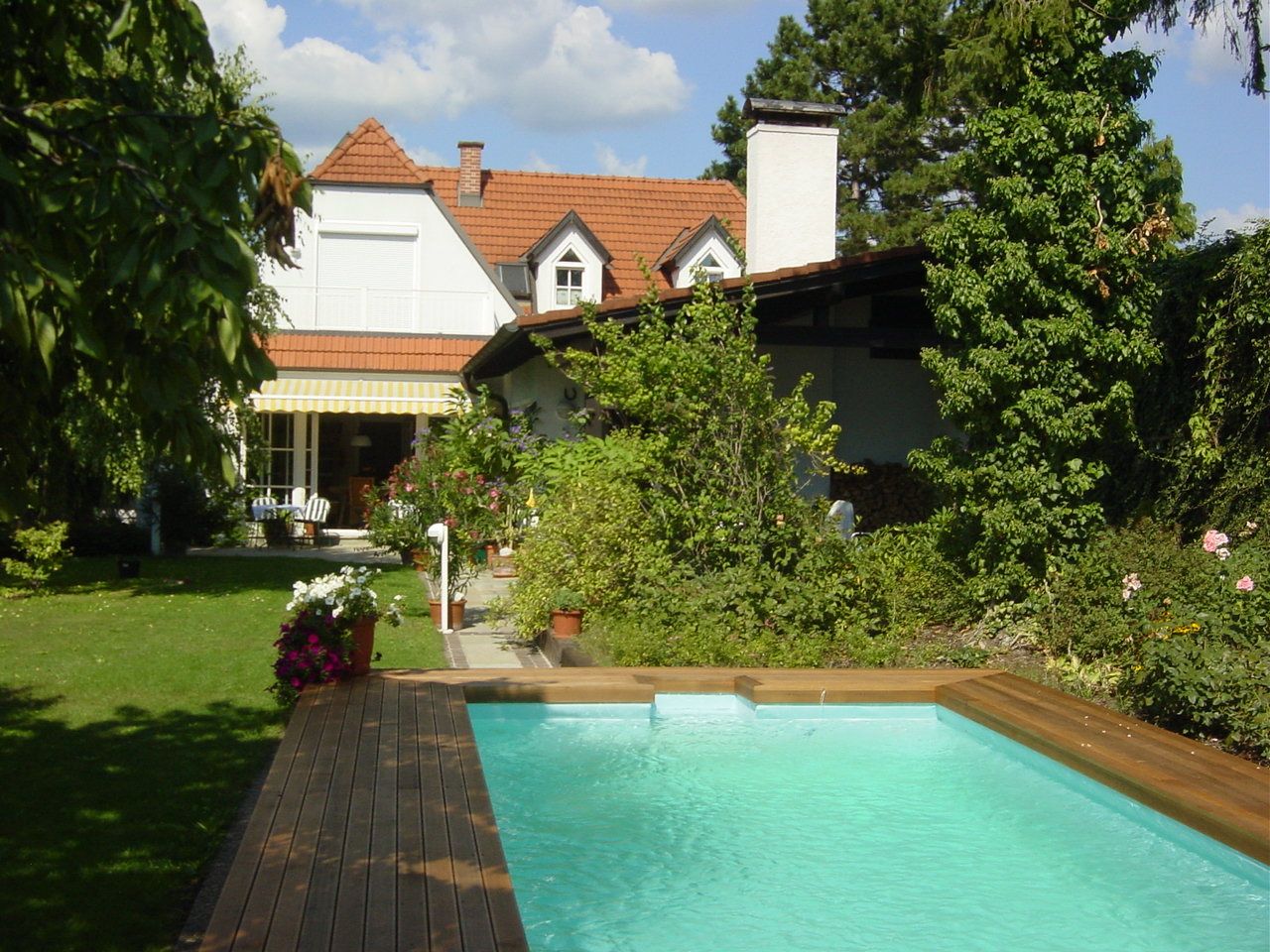 Ein Garten mit einem Pool, umgeben von Pflanzen und einem Haus im Hintergrund.
