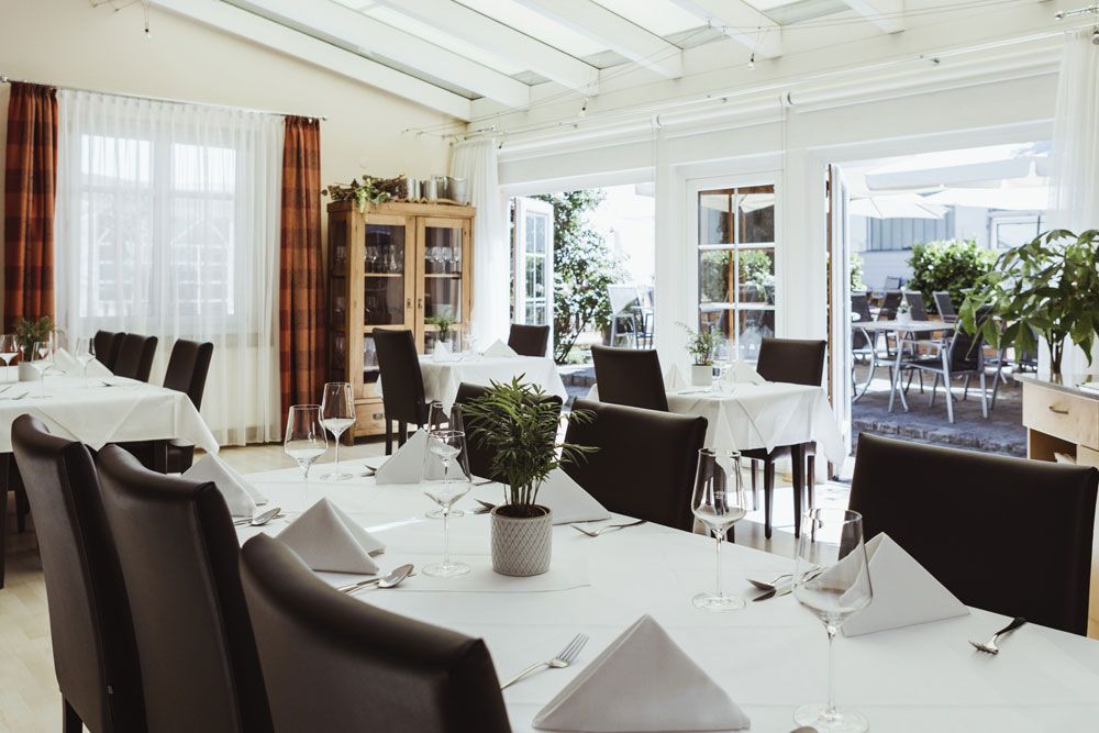 Elegantes Restaurant mit weißen Tischdecken und Glasfront zur Terrasse.
