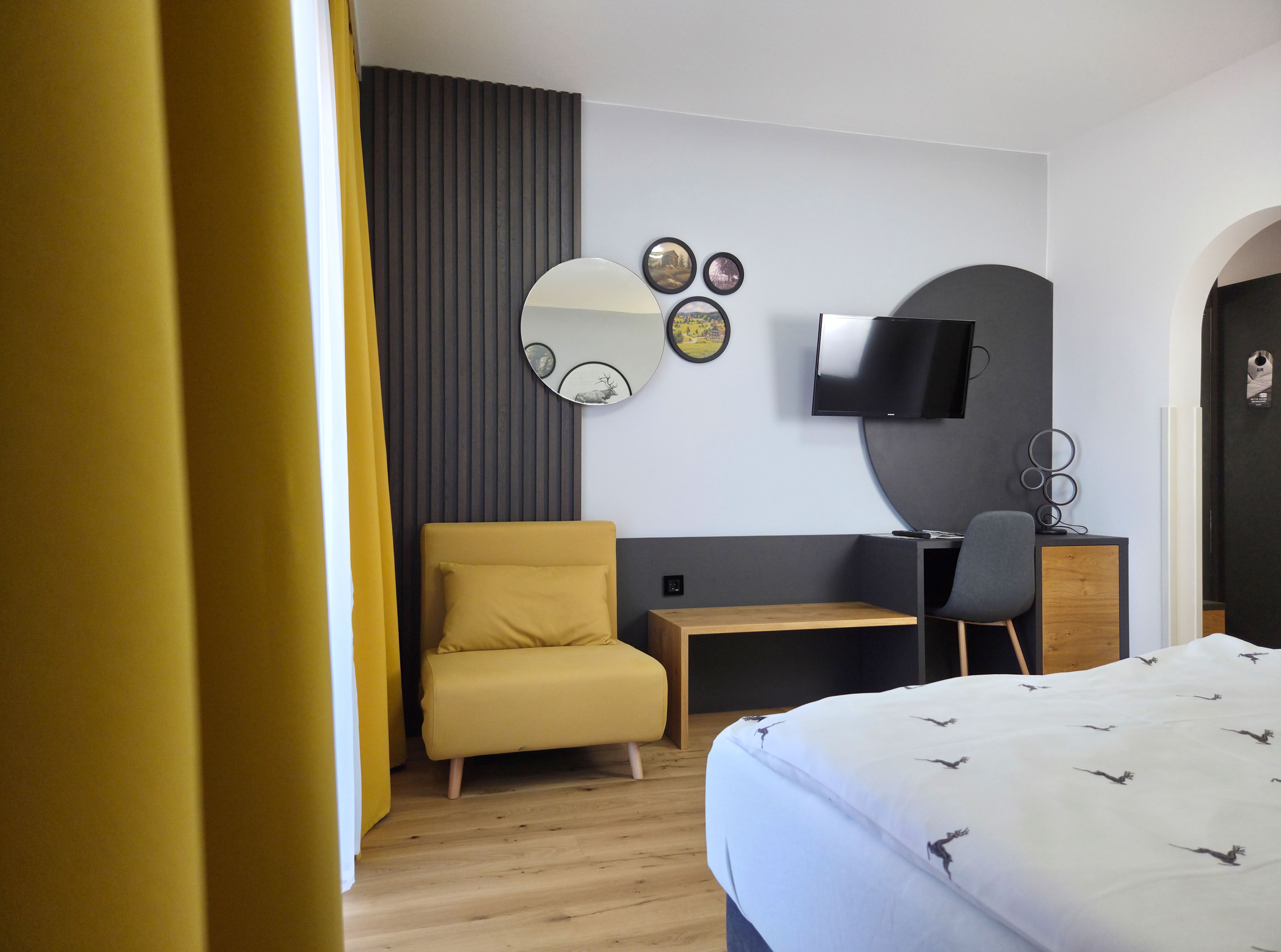 Modern eingerichtetes Zimmer mit gelbem Sessel, Spiegeln an der Wand, einem Fernseher und einem Schreibtisch mit Stuhl.