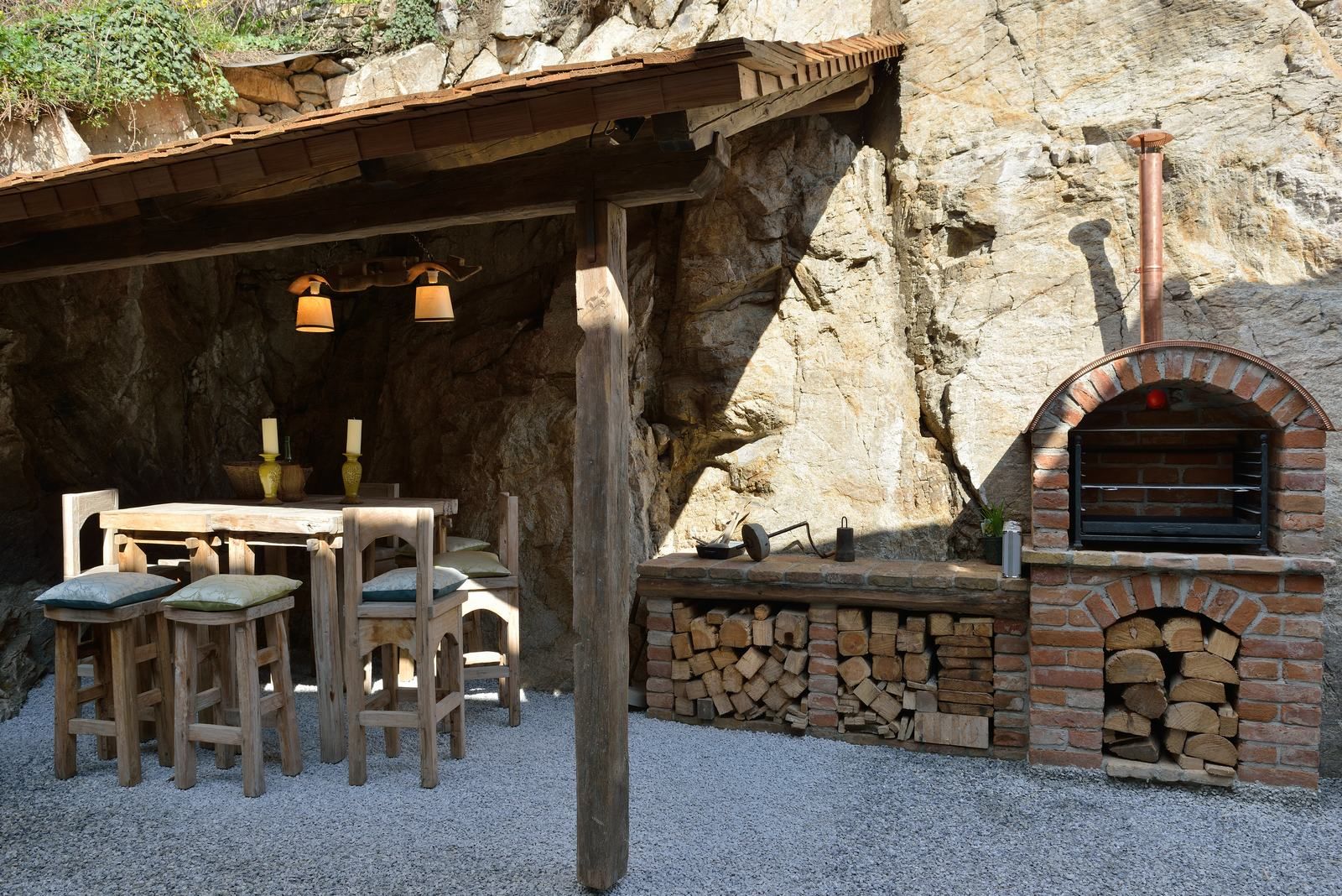 Rustikaler Außenbereich mit Holztisch, Stühlen und gemauertem Ofen.