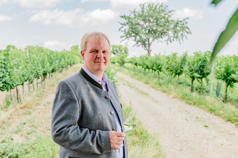 Mann in traditioneller Kleidung mit Weinglas in einem Weinberg.