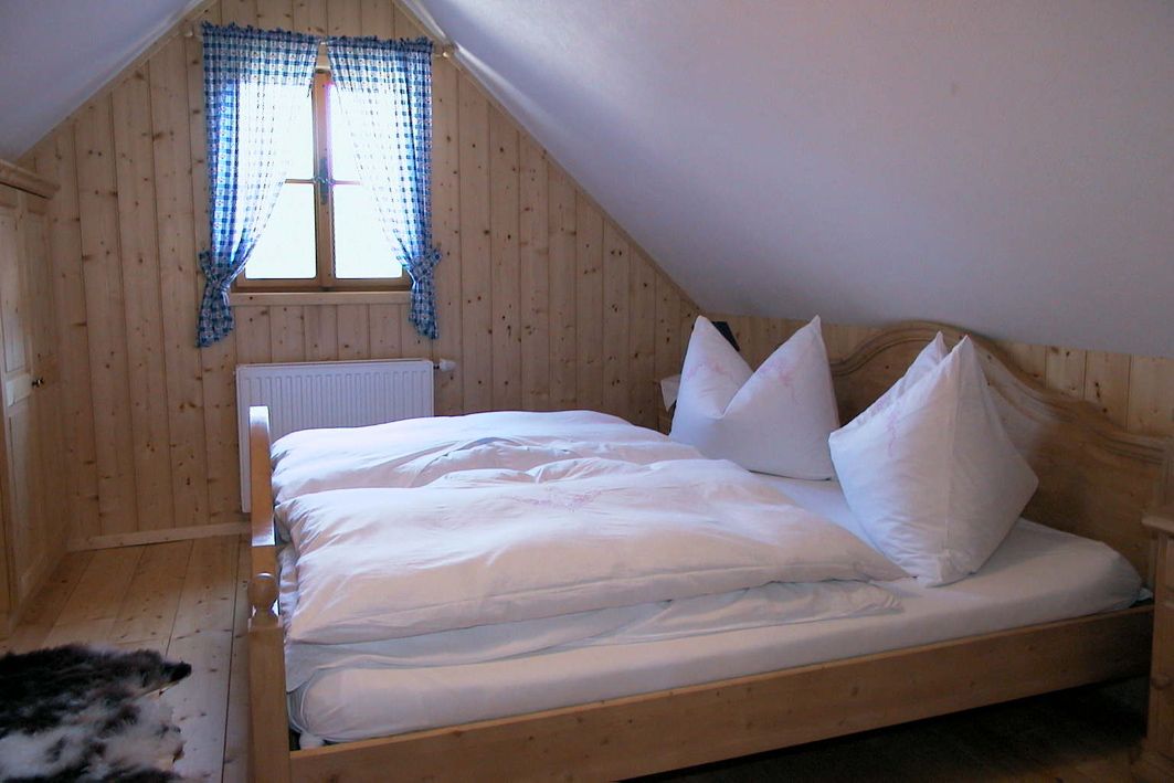 Gemütliches Schlafzimmer mit Holzwänden, einem Doppelbett und einem Fenster mit blau karierten Vorhängen.