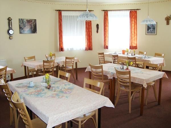 Ein gemütlicher Frühstücksraum mit mehreren gedeckten Tischen und Holzstühlen, dekoriert mit Blumen und Bildern an den Wänden.