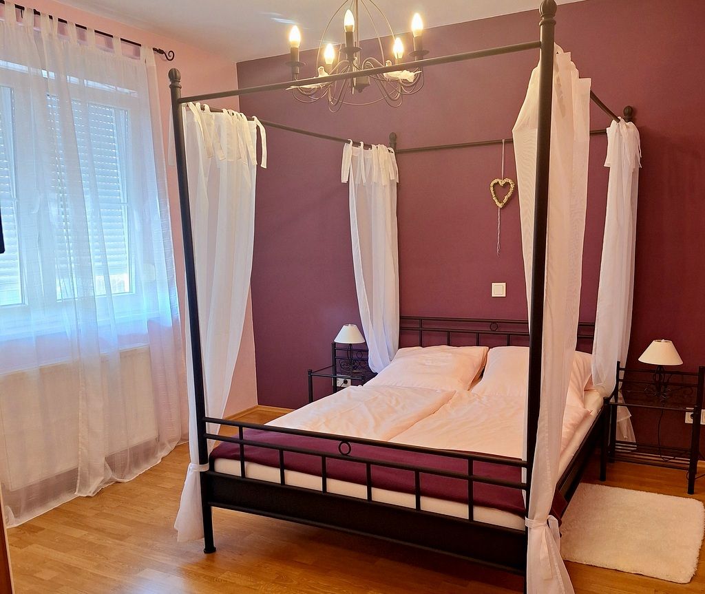 Schlafzimmer mit Himmelbett, lila Wänden und weißen Vorhängen.