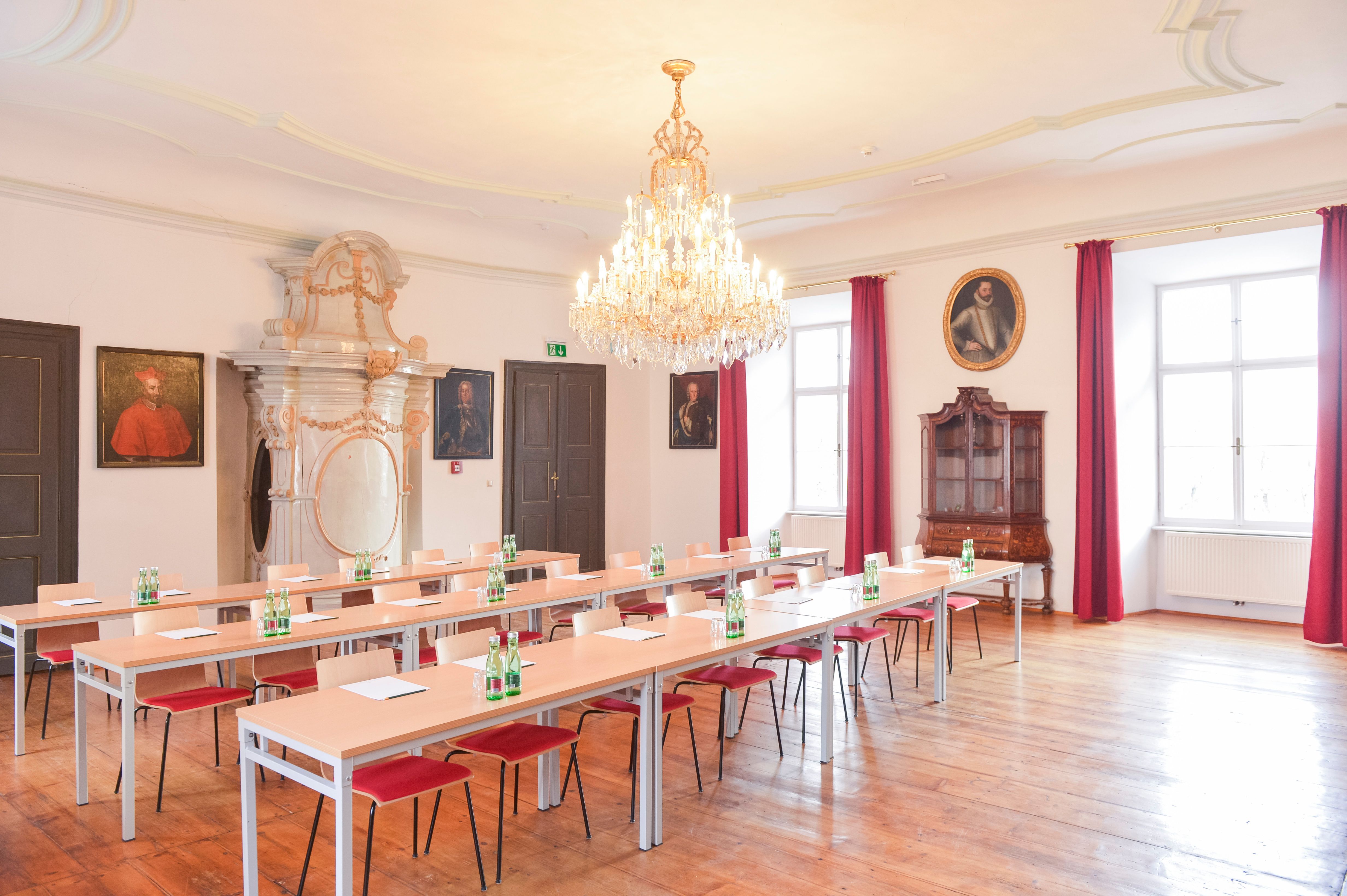 Eleganter Seminarraum mit Kronleuchter, Holzboden und Porträts an den Wänden.