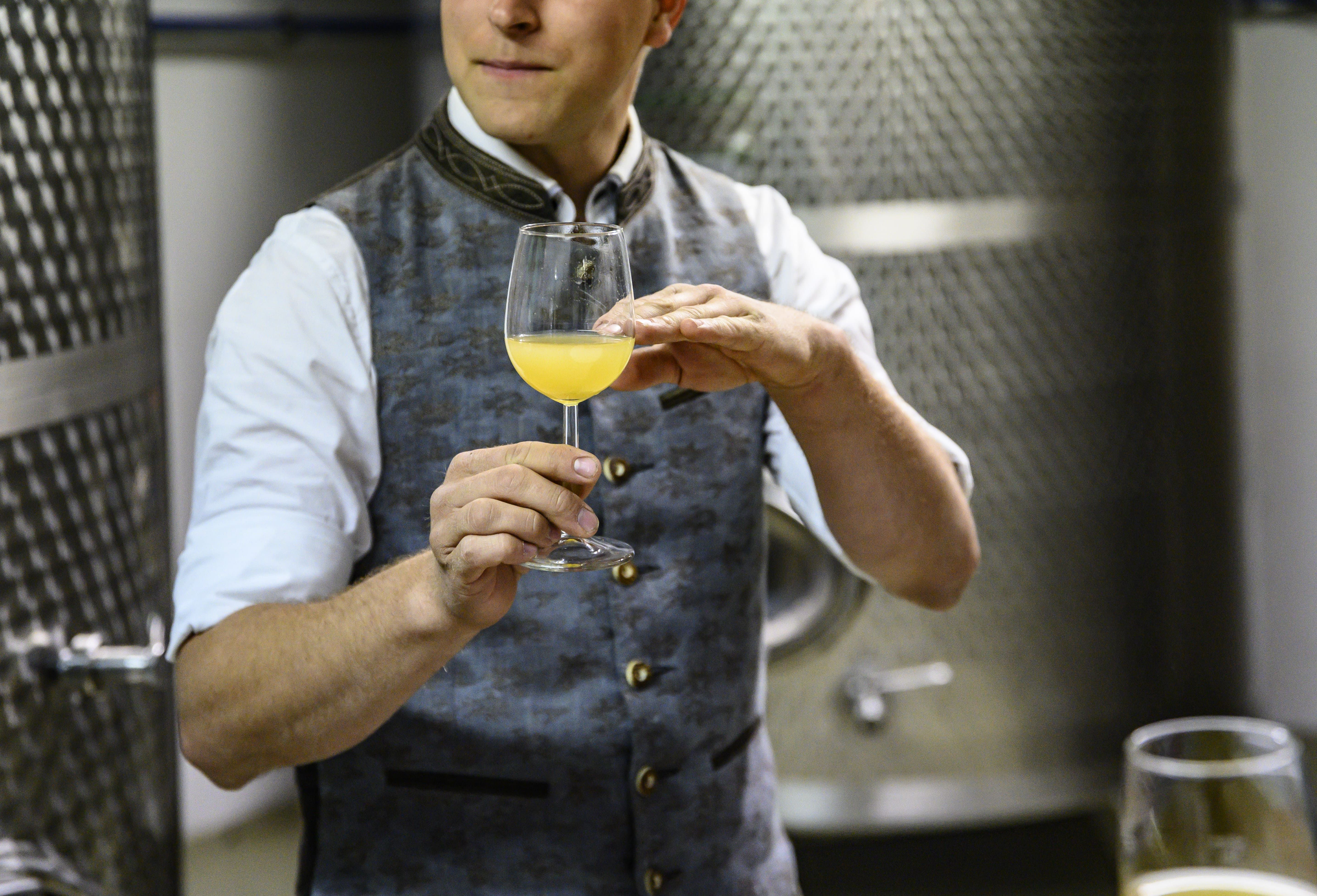 Person in traditioneller Kleidung hält ein Glas mit Most in der Hand