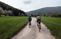 Zwei Radfahrer gleiten entspannt auf einem schmalen Schotterweg durch die malerische Landschaft der Wiener Alpen. Umgeben von saftigem Grün und majestätischen Bergen, erleben sie die Freiheit und die Schönheit der Natur in vollen Zügen. Der Duft von frischem Gras und die sanfte Brise machen diese Radtour zu einem unvergesslichen Erlebnis.