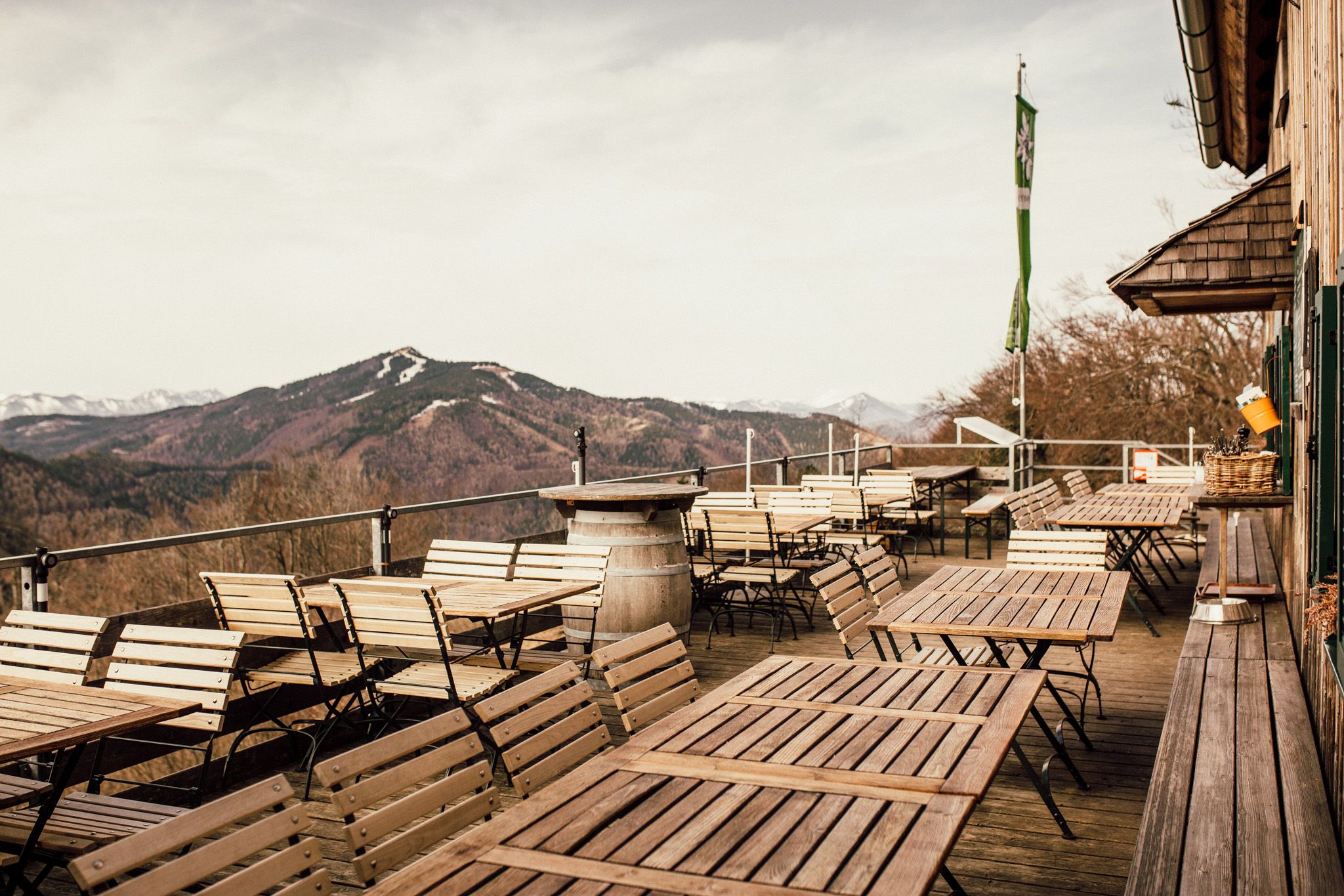 Leere Terrasse mit Holztischen und -stühlen, Berglandschaft im Hintergrund.