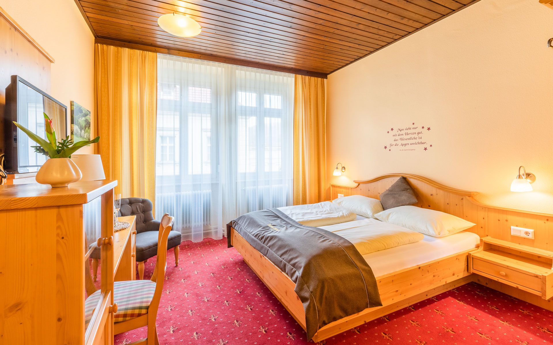 Gemütliches Hotelzimmer mit Doppelbett, Holzmöbeln und rotem Teppich.
