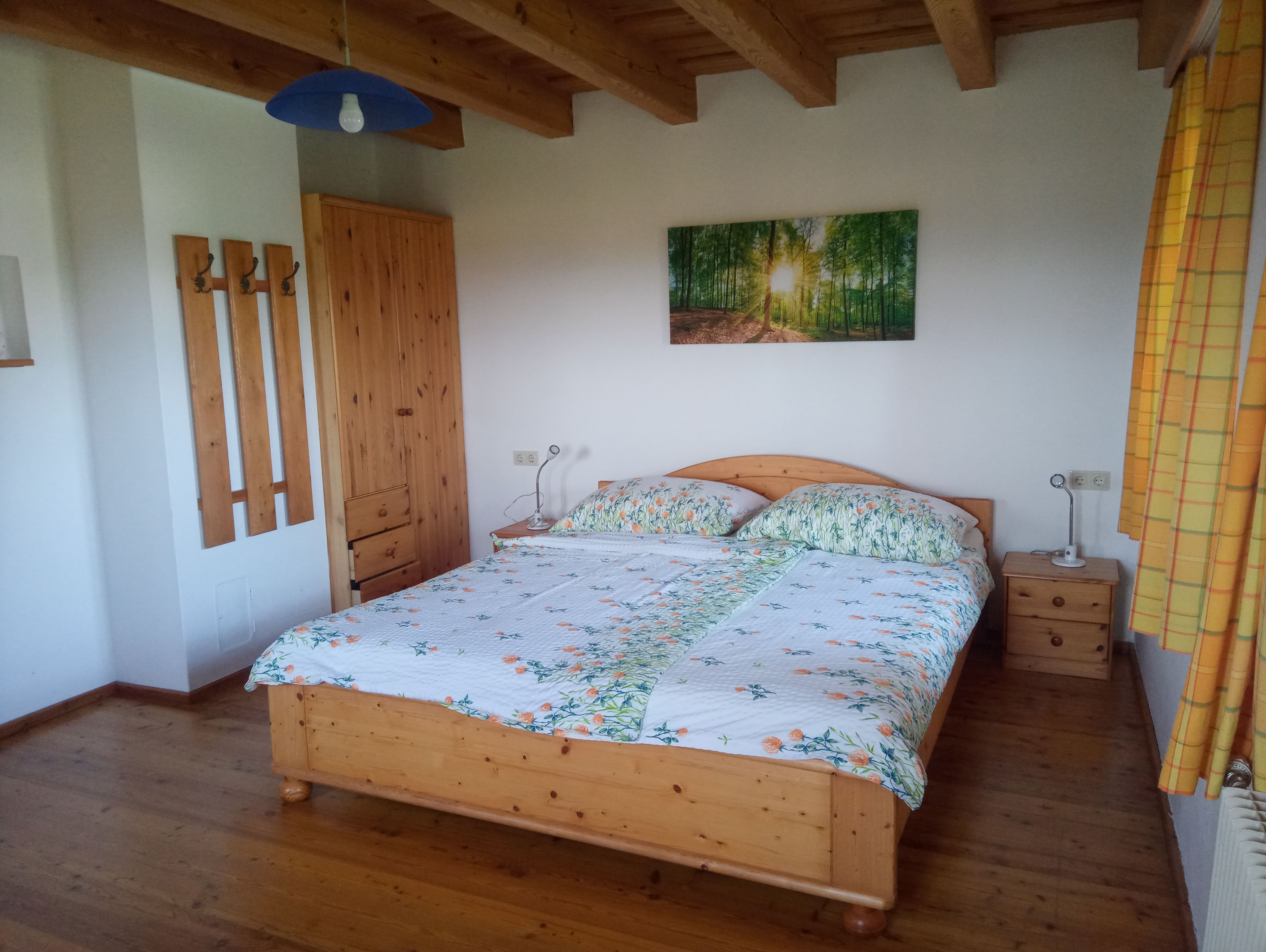 Schlafzimmer mit Holzbett, Nachttischen, Kleiderschrank und Wandbild eines Waldes.