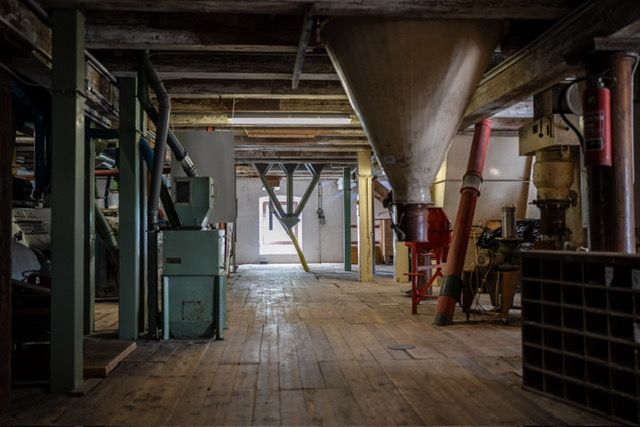 Innenansicht einer alten Mühle mit Holzboden und Maschinen.
