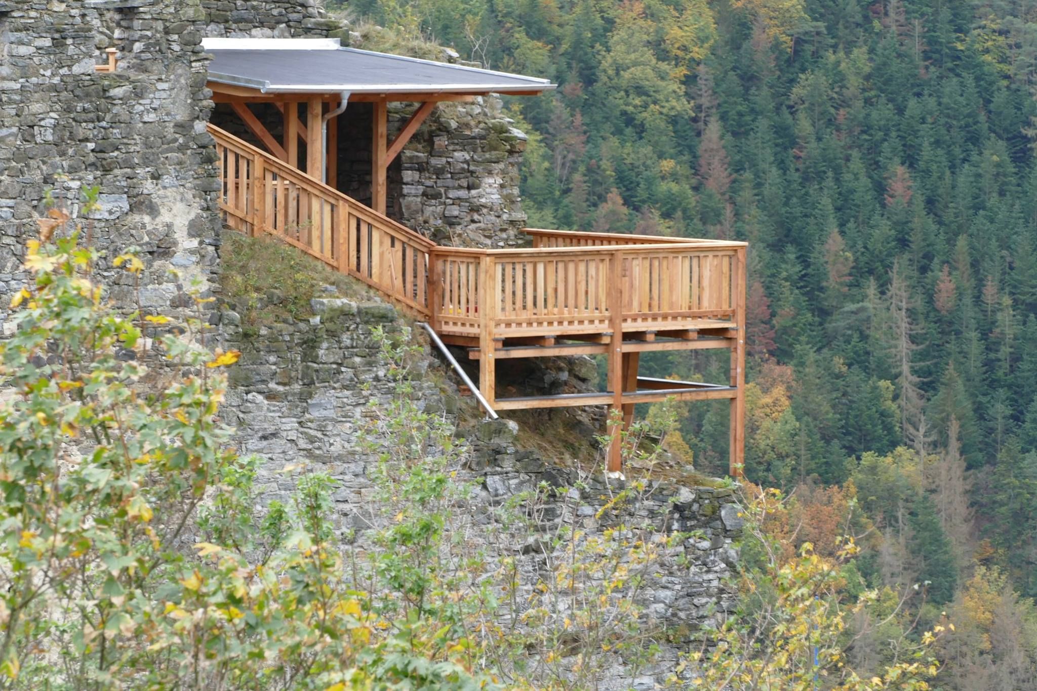 Holzplattform an einer Burgruine mit Wald im Hintergrund.