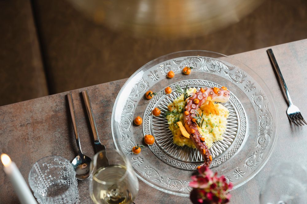 Elegantes Gericht mit Oktopus und Beilage auf gläsernem Teller serviert.