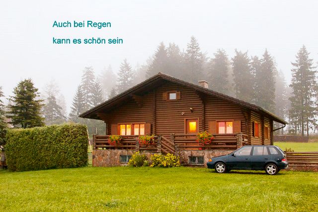 Blockhaus im Nebel mit Auto und Bäumen im Hintergrund.