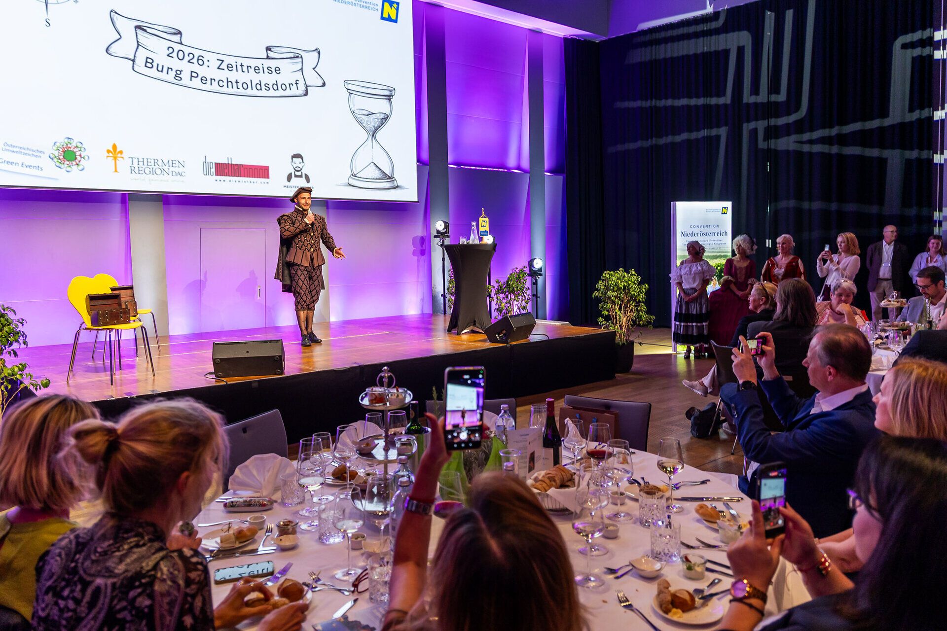 Blick auf den Galaabend zum 20-jährigen Jubiläum des Convention Bureau Niederösterreich im Großen Burgsaal der Burg Perchtoldsdorf: Ein Künstler steht auf der Bühne, während die Gäste an gedeckten Tischen das Programm verfolgen.