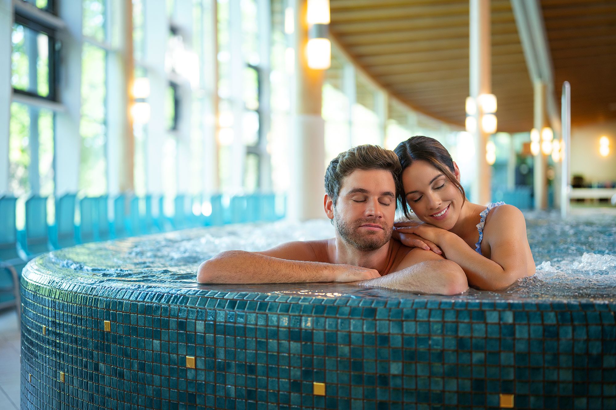 Ein Paar entspannt sich in einem Whirlpool in einem modernen Spa mit großen Fenstern.