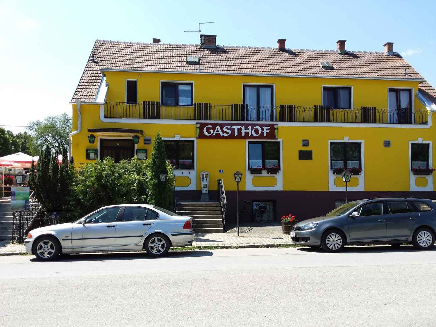 Gelbes Gebäude mit der Aufschrift 'Gasthof', zwei Autos davor geparkt.
