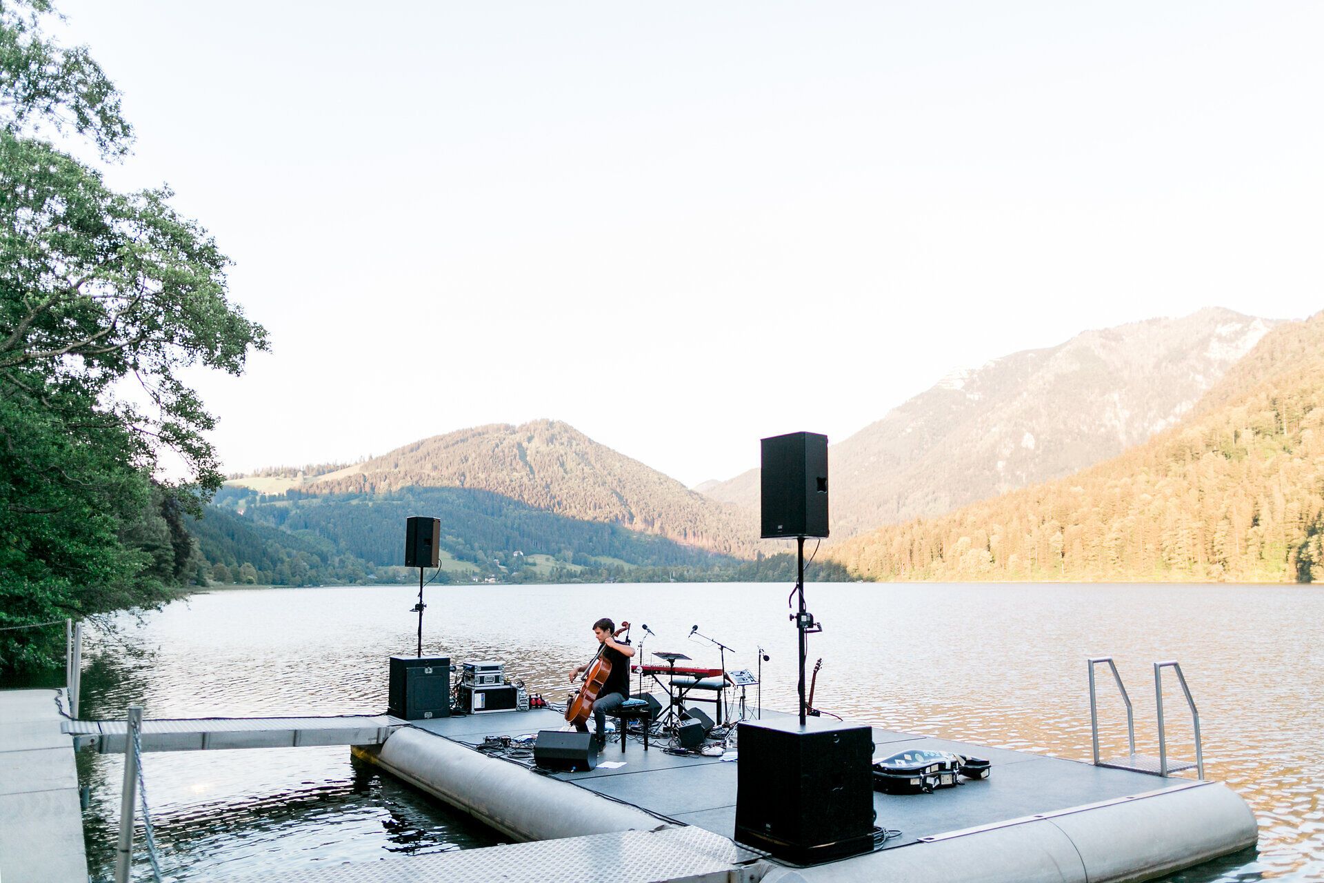 Musiker spielt auf einem Steg am Lunzer See mit einem Instrument, im Hintergrund der See und die Berglandschaft