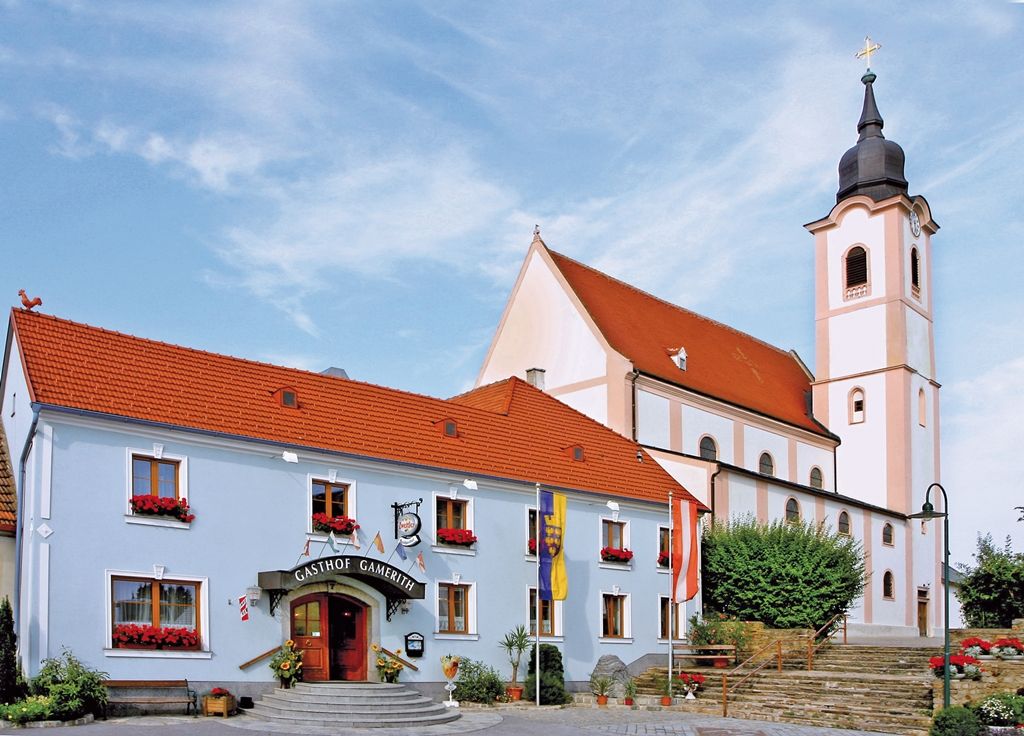 Gasthaus Gamerith neben einer Kirche mit Turm und rotem Dach.