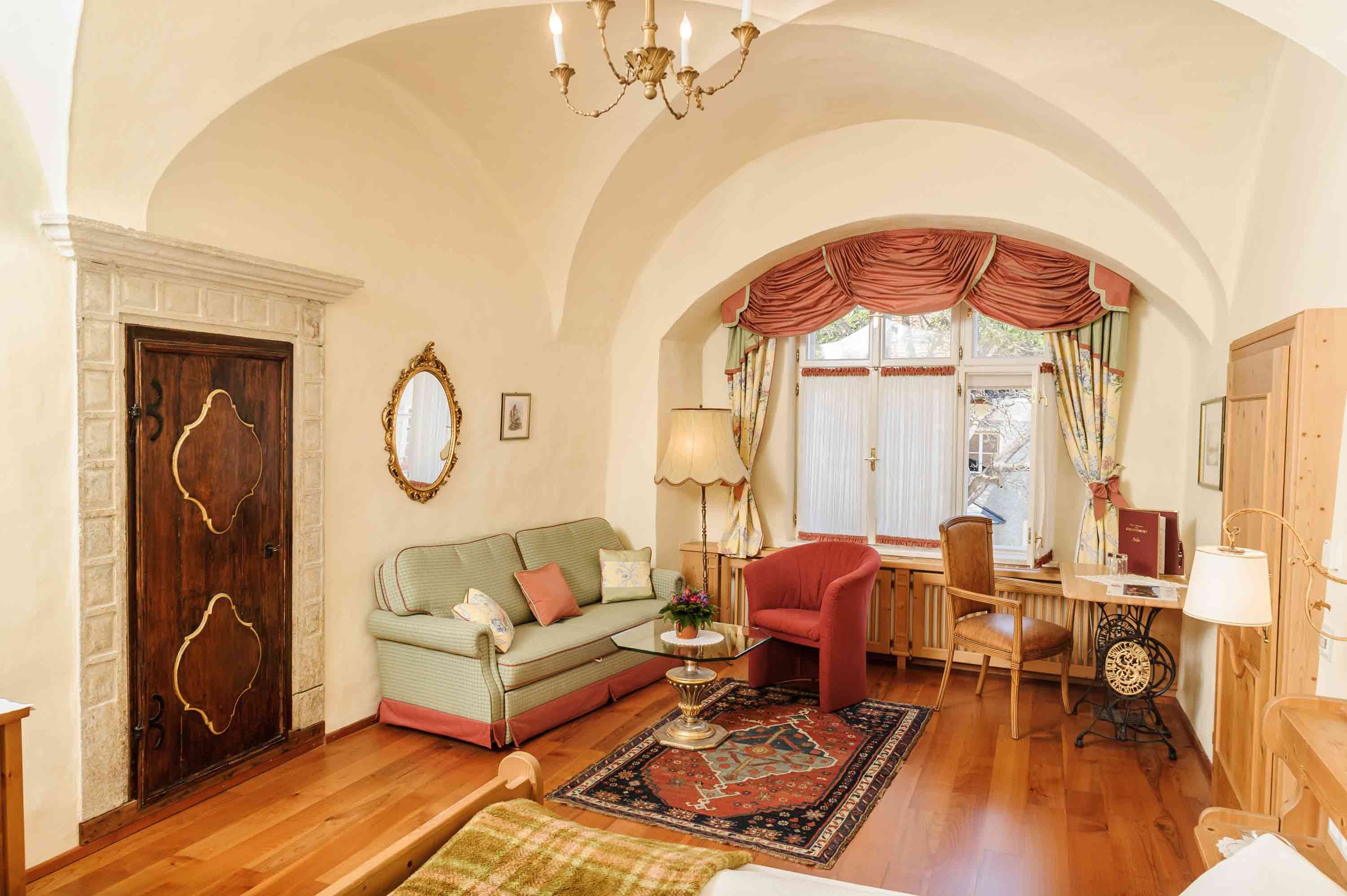 Gemütliches Wohnzimmer mit antikem Flair, Sofa, Teppich, Tisch und Fenster mit Vorhängen.