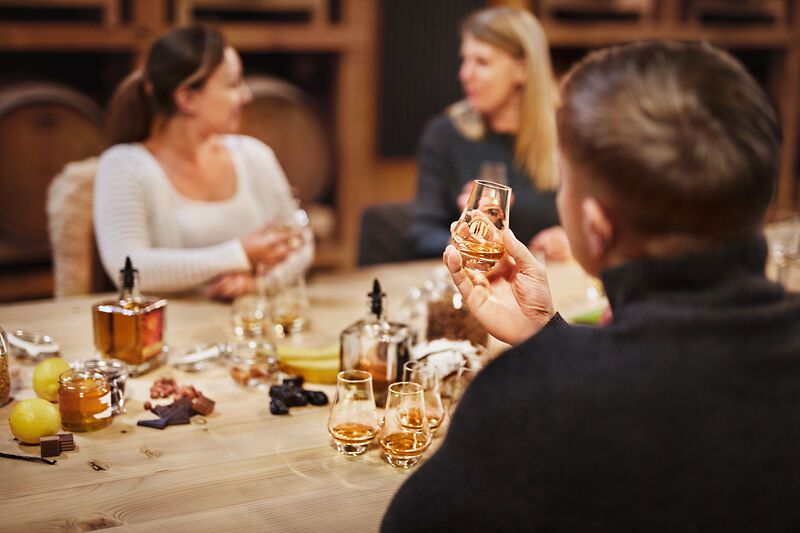 Personen bei einer Whisky-Verkostung an einem Tisch mit Gläsern und Zutaten.