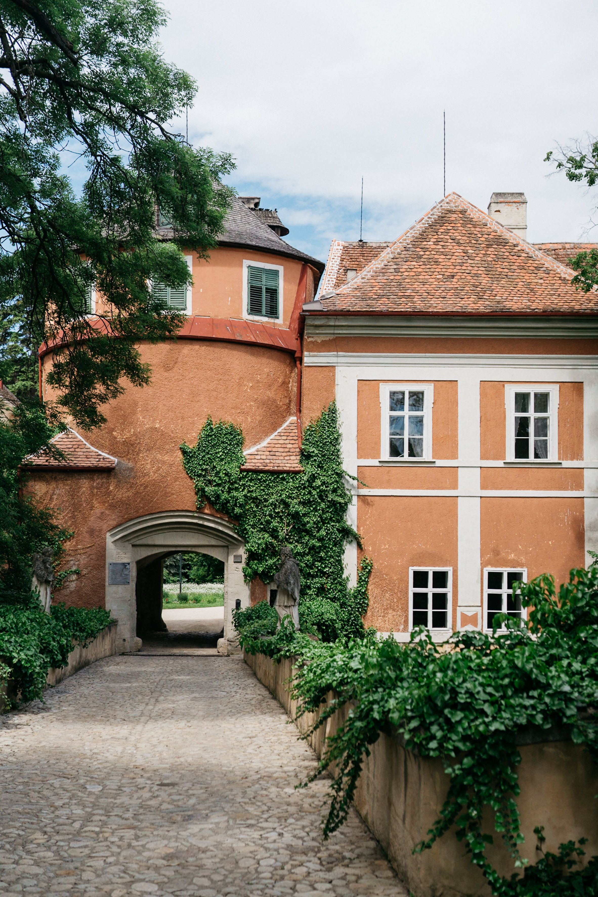 Eingangstor von Schloss Schrattenthal mit bewachsener Fassade und gepflastertem Weg.