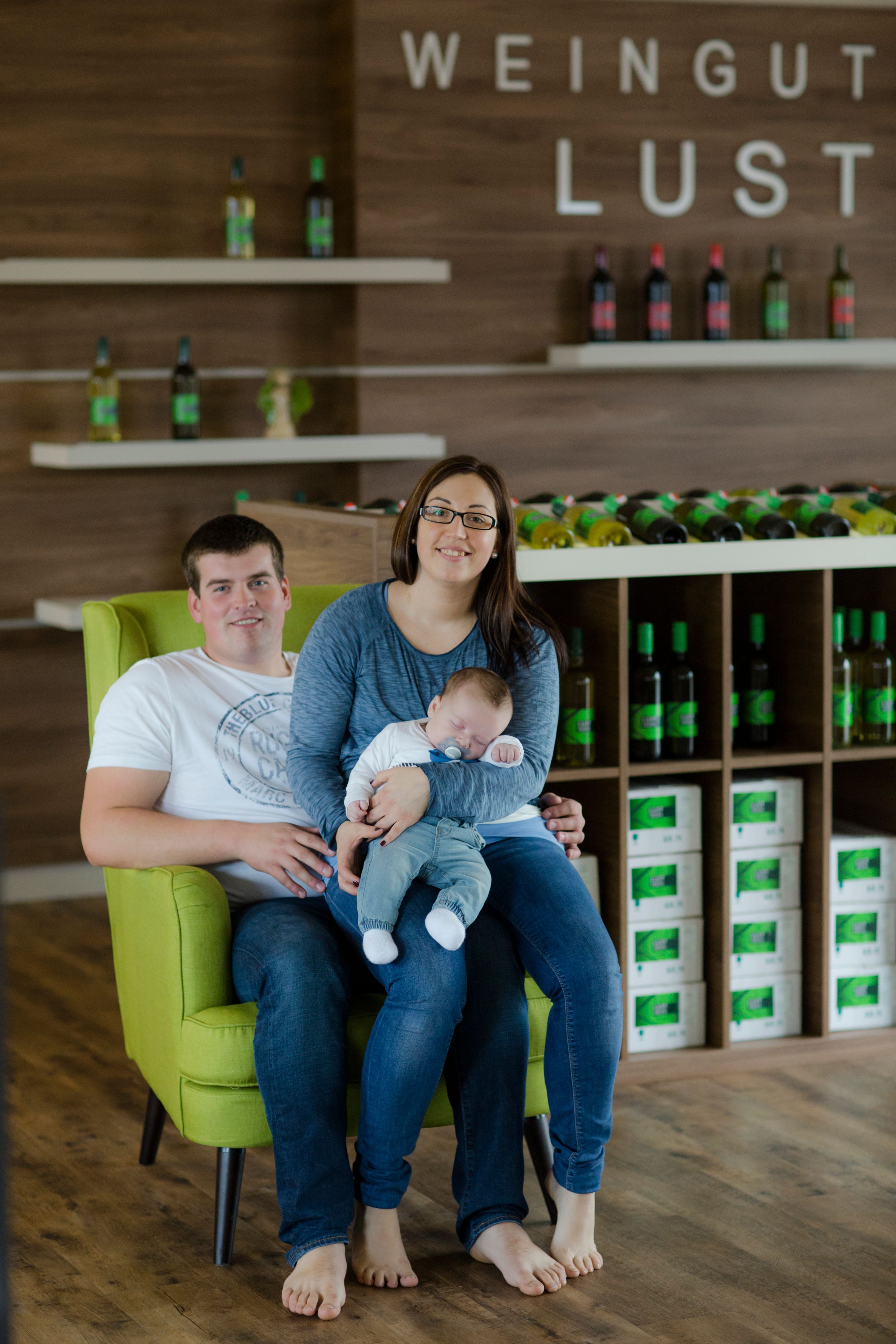 Ein Paar mit einem Baby sitzt auf einem grünen Sessel in einem Weingut.