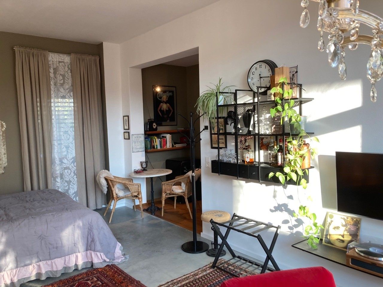 Gemütliches Wohnzimmer mit Bett, Regal, Pflanzen und Wanddekoration.