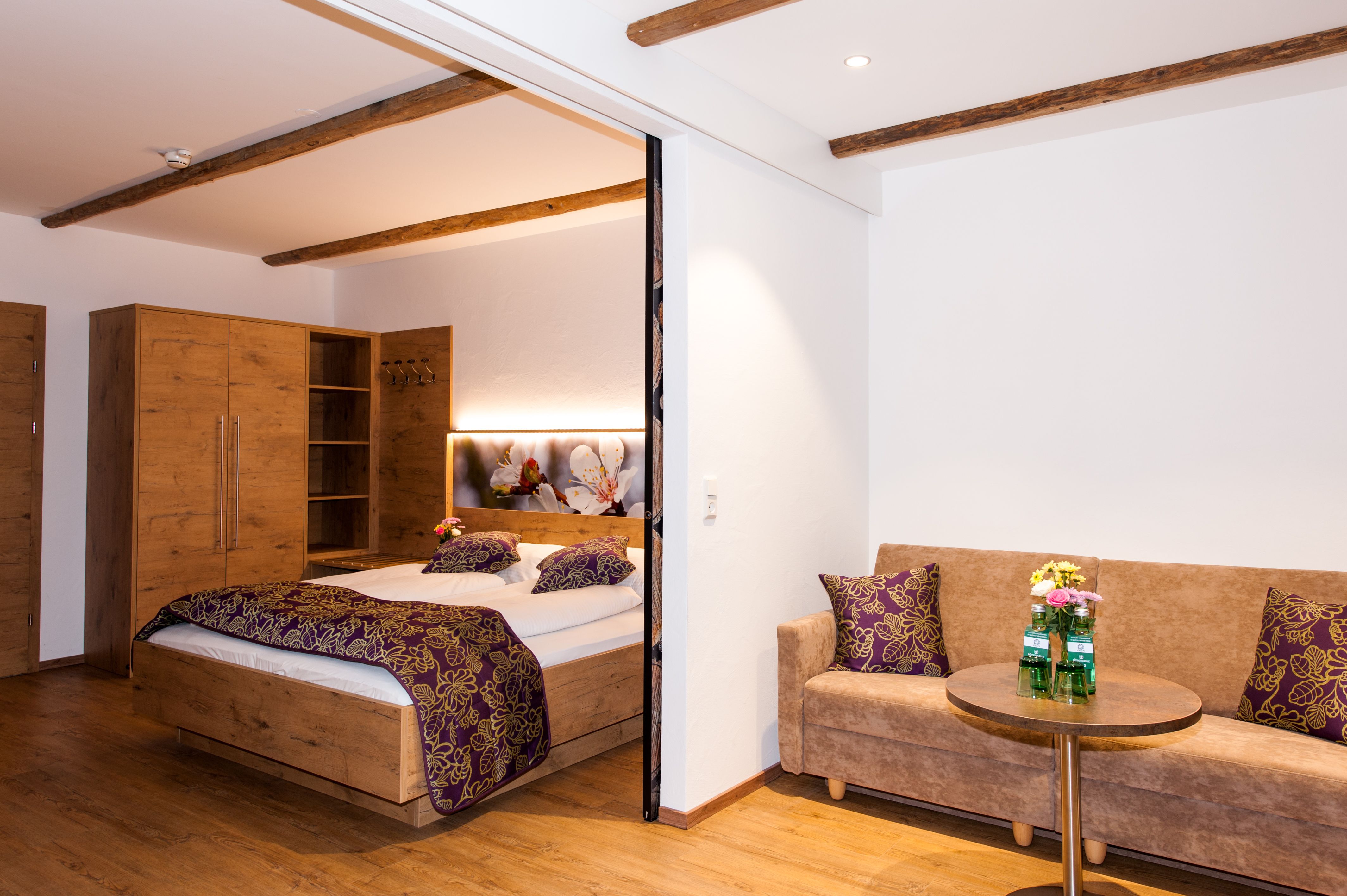 Gemütliches Hotelzimmer mit Holzmöbeln, Doppelbett, Sofa und kleinem Tisch.