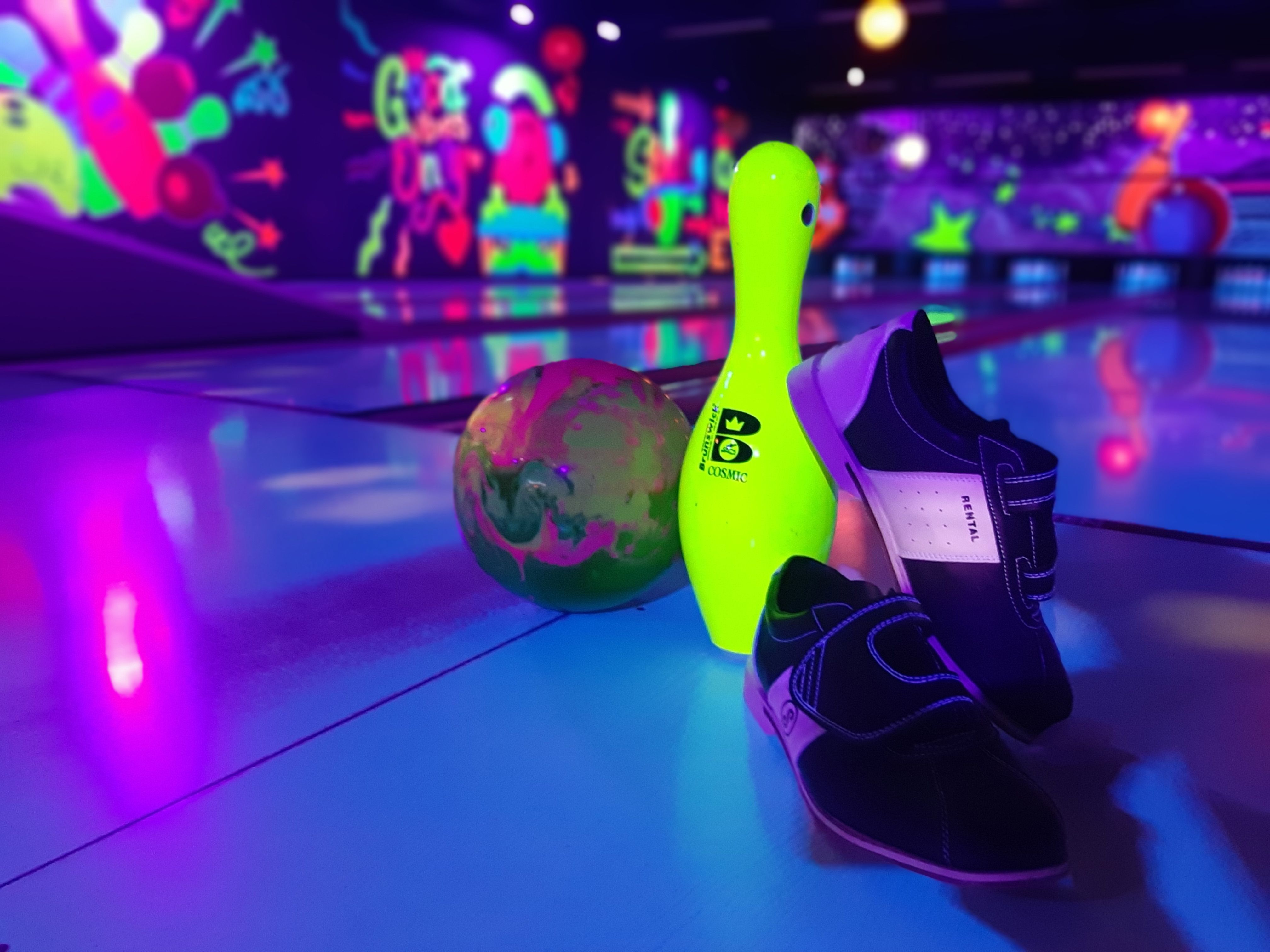 Bowlingkugel, Kegel und Schuhe auf einer Bowlingbahn mit neonfarbener Beleuchtung.
