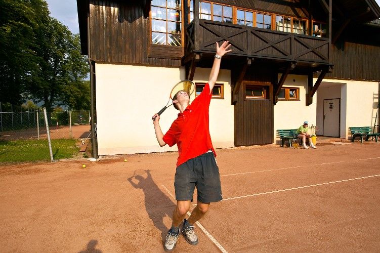 Person beim Tennisspielen vor einem Gebäude.